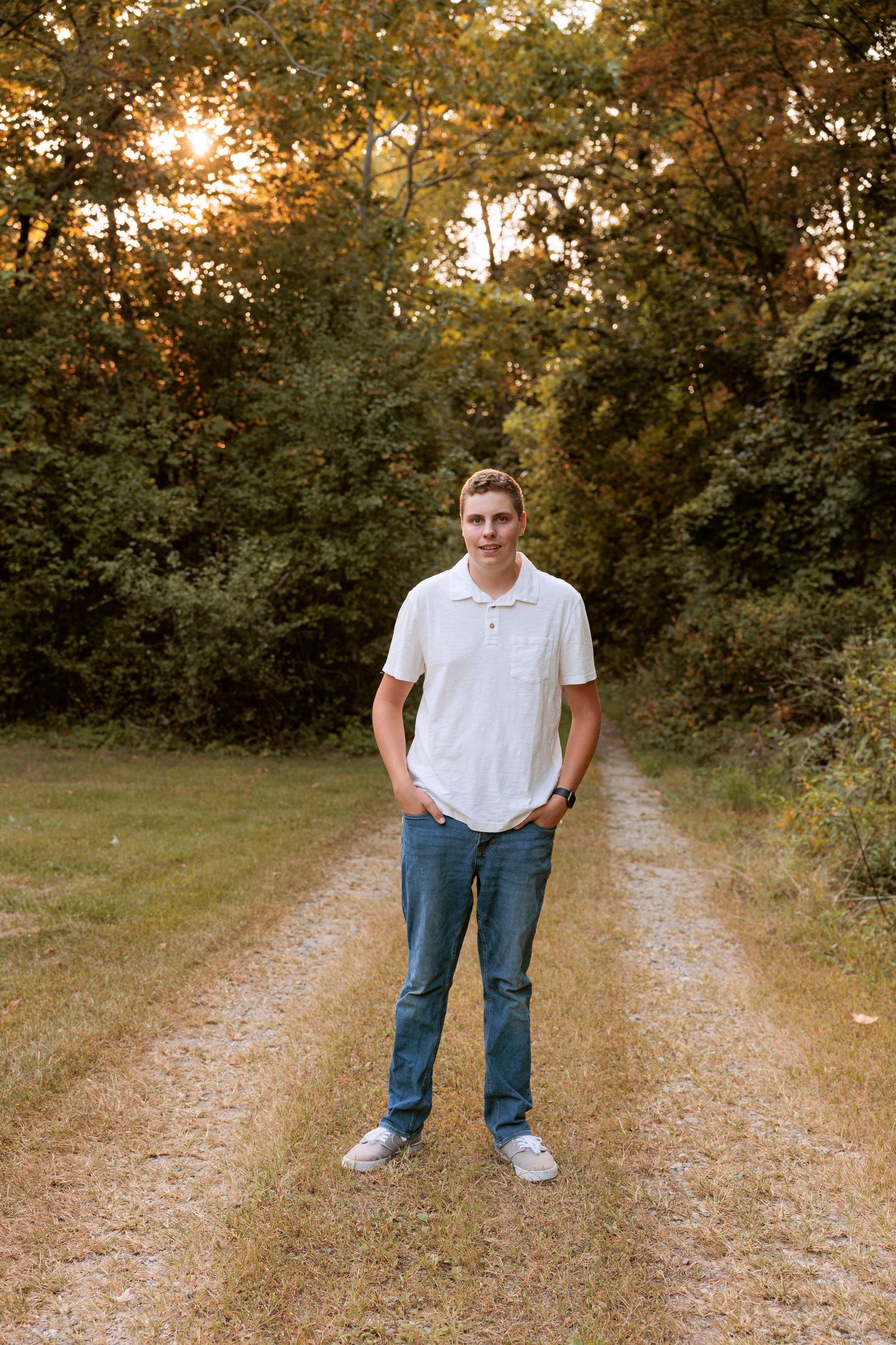 A full-length portrait on a nature trail during golden hour with trees in the background.