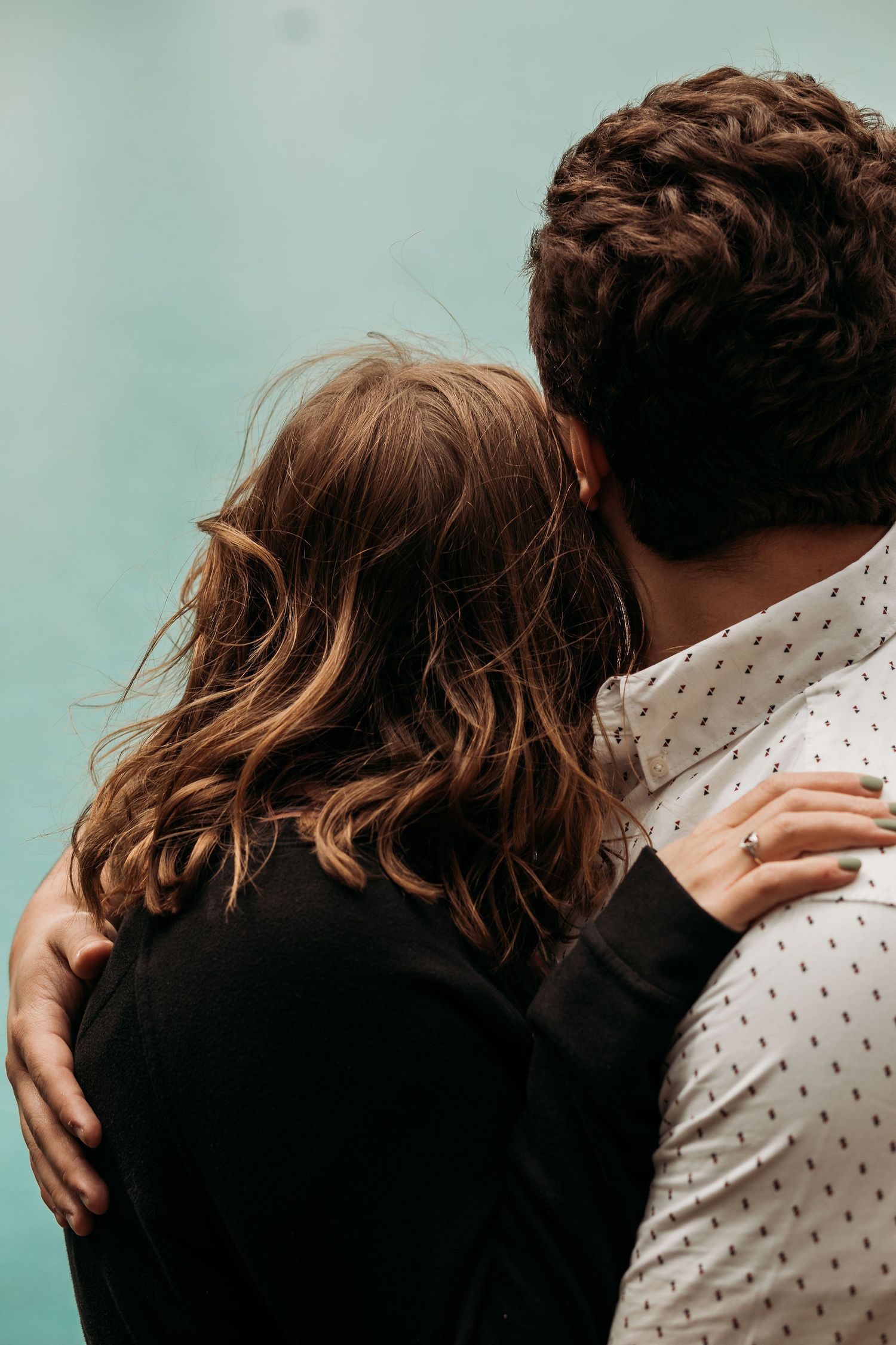 Intimate close-up of couple embracing against turquoise mountain lake backdrop.