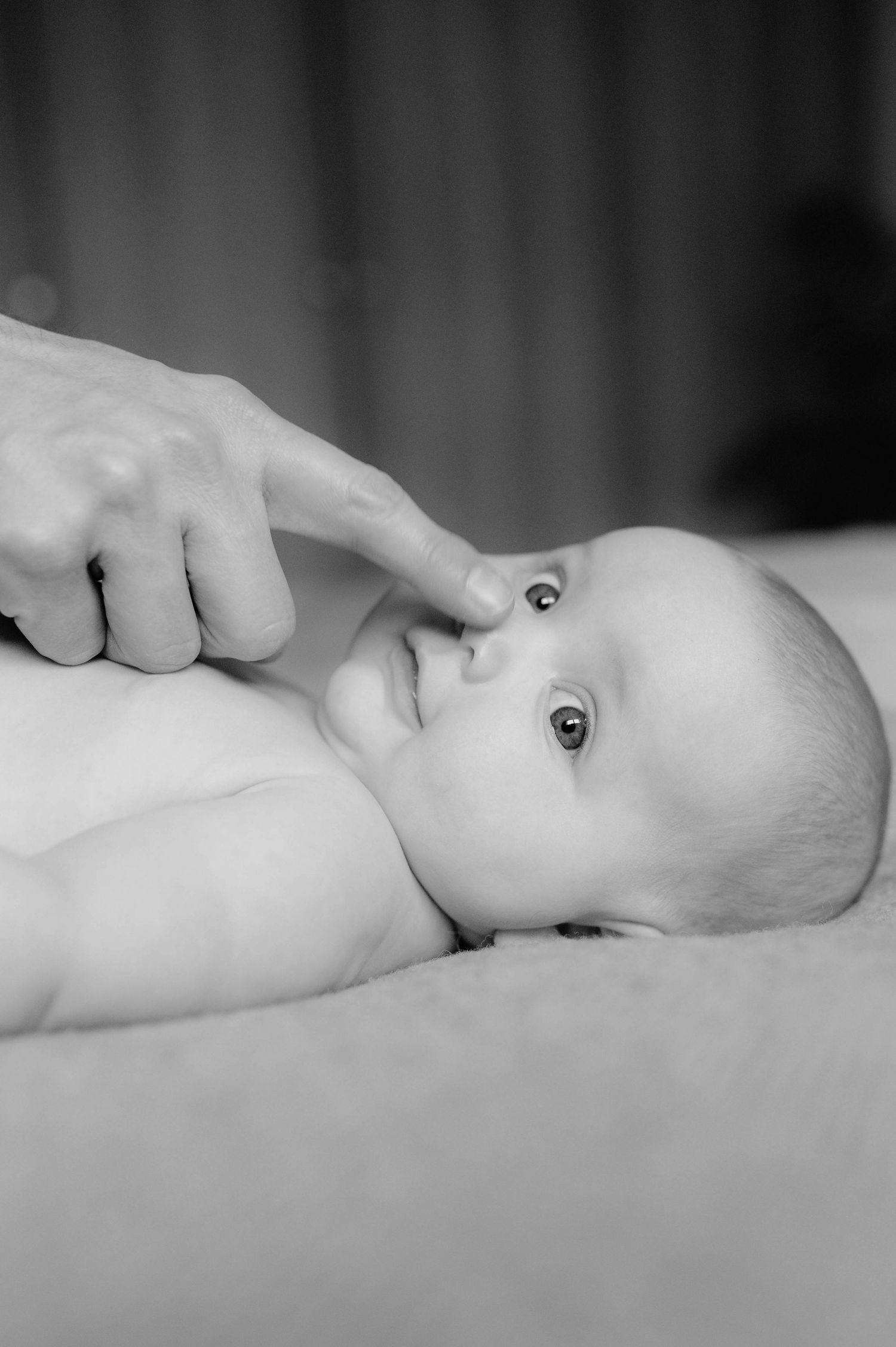 A tender moment captured in black and white as a gentle hand touches an infant lying on soft bedding.