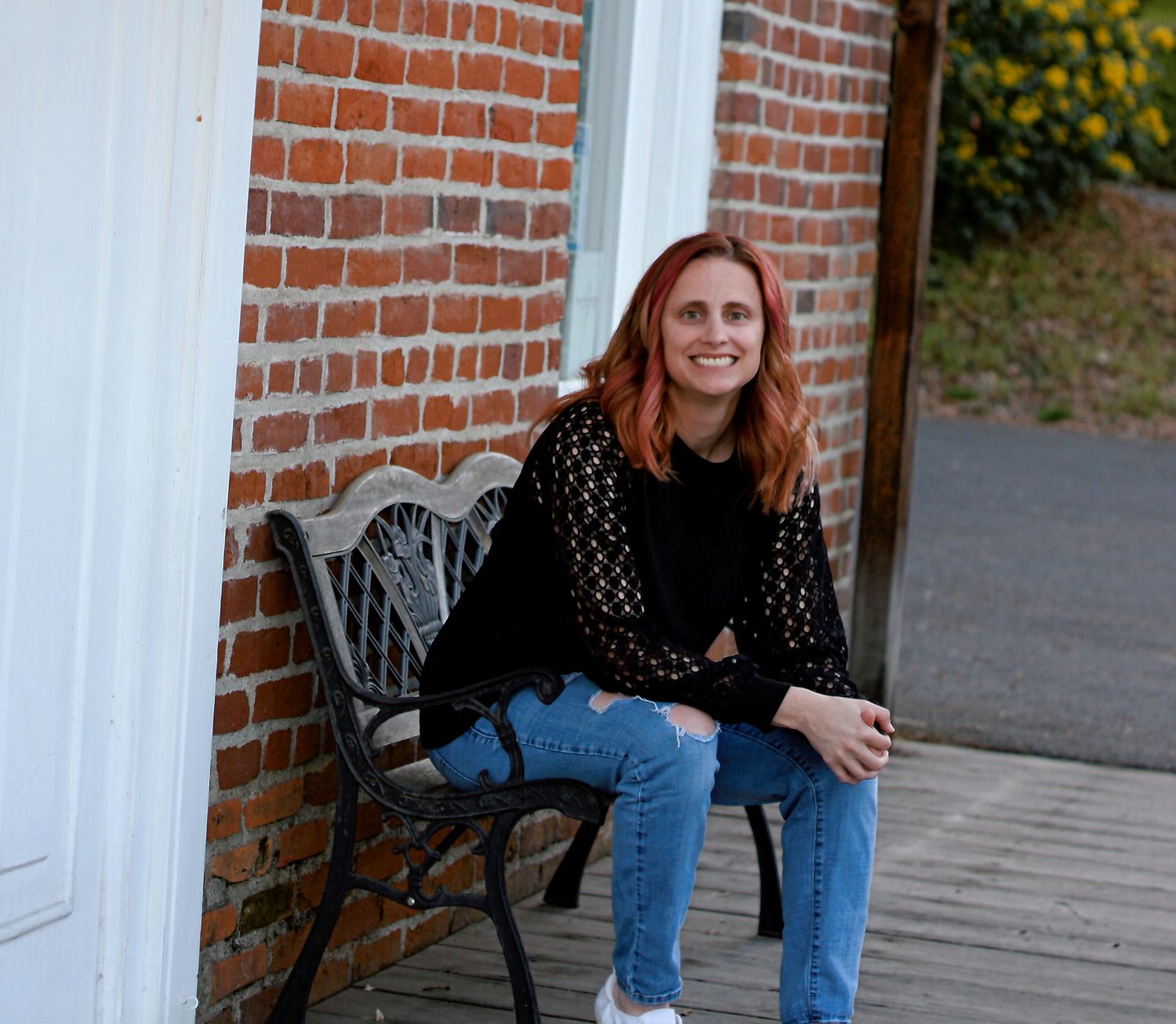A woman wearing jeans and a dark top sits casually on outdoor brick steps.