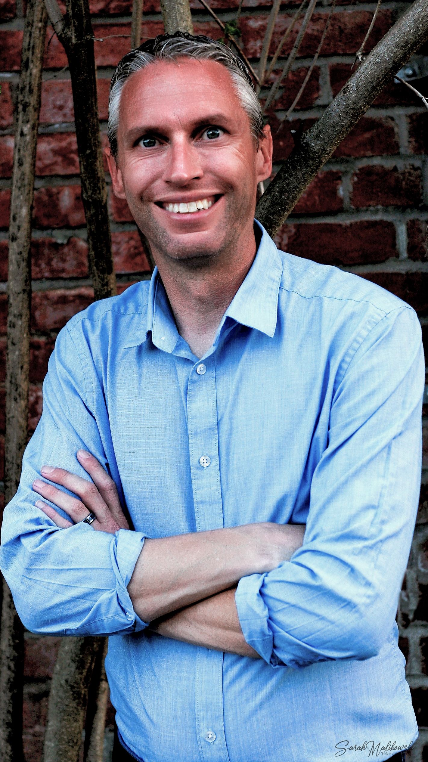 A series of headshots against a brick wall shows a person in a light blue button-down shirt.