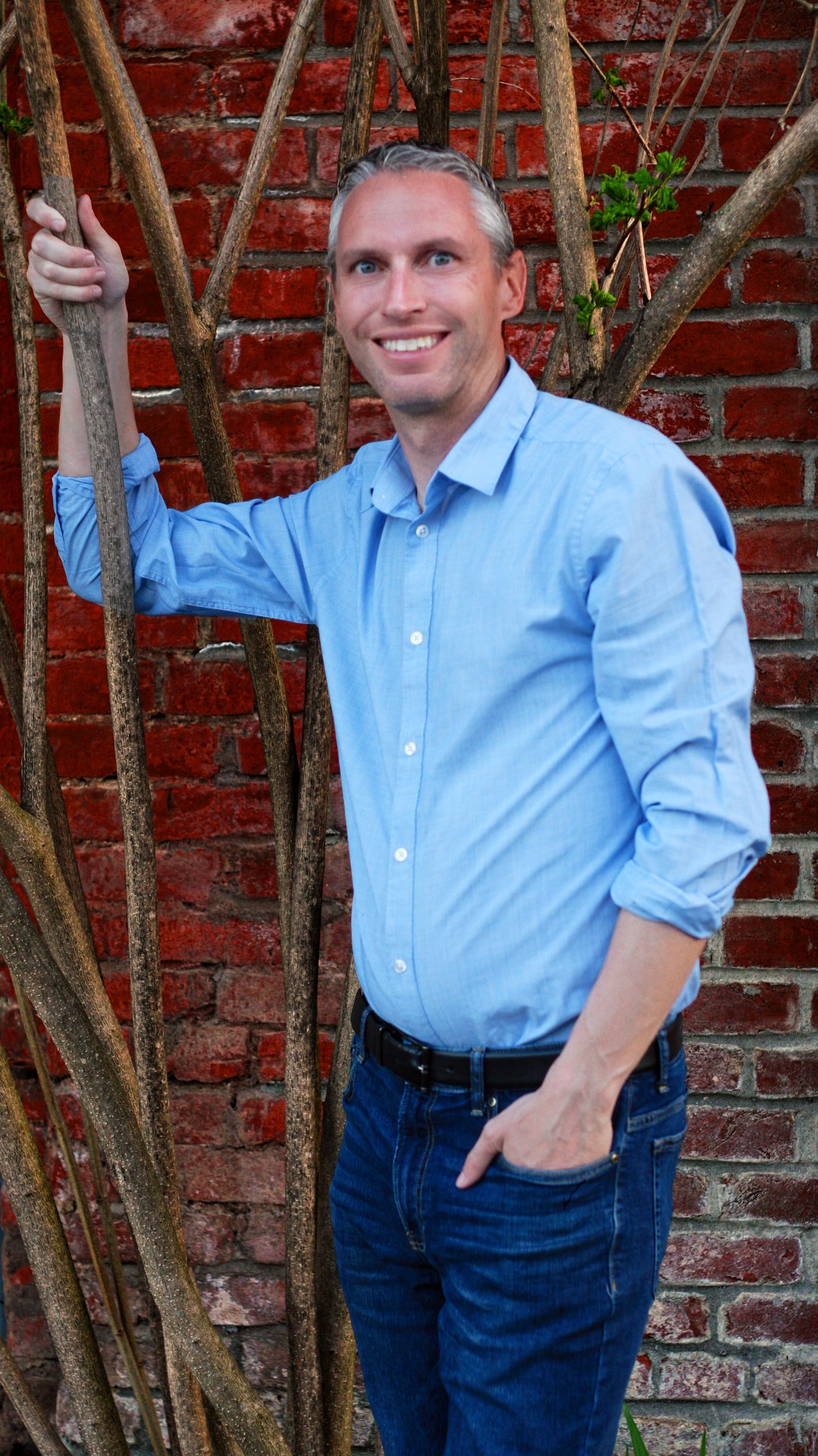Professional portraits against a brick wall feature someone in a blue shirt and jeans striking various poses.