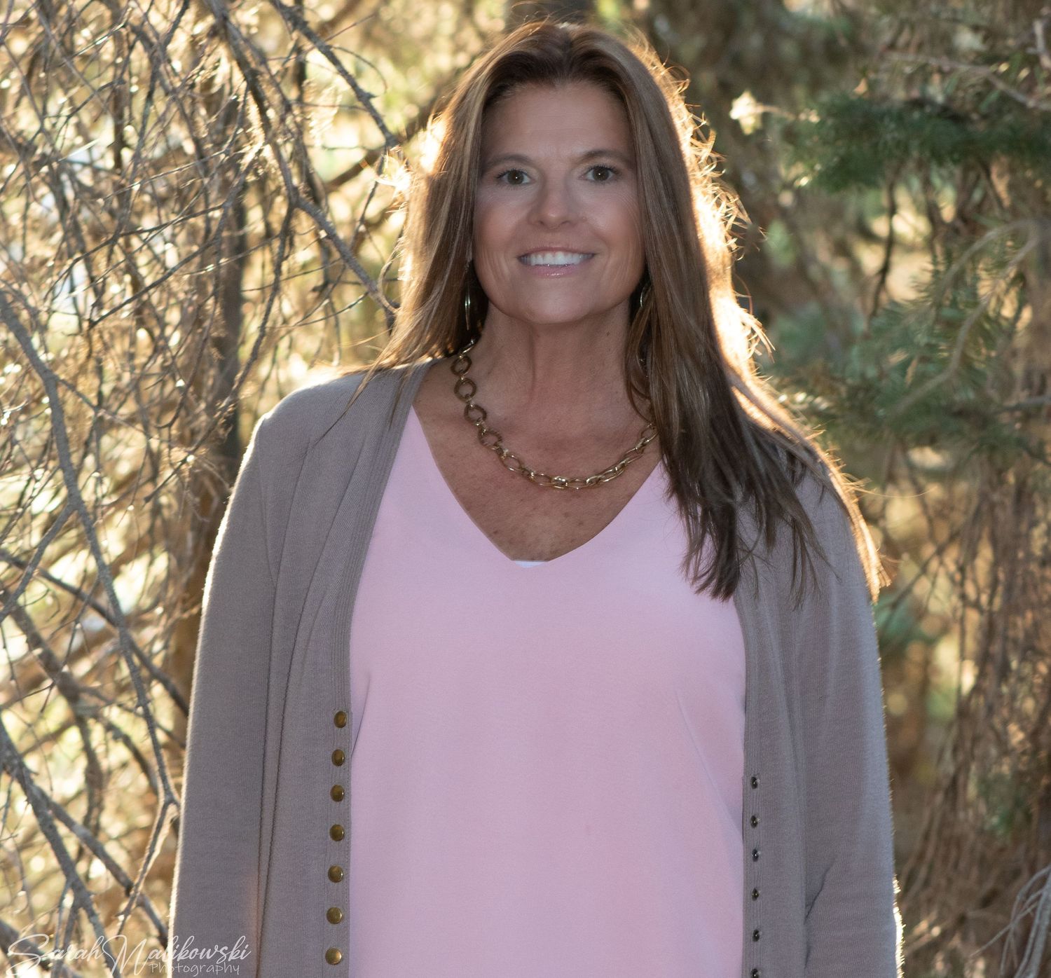 Casual outdoor portrait featuring a pink tank top and beige cardigan with layered necklaces.