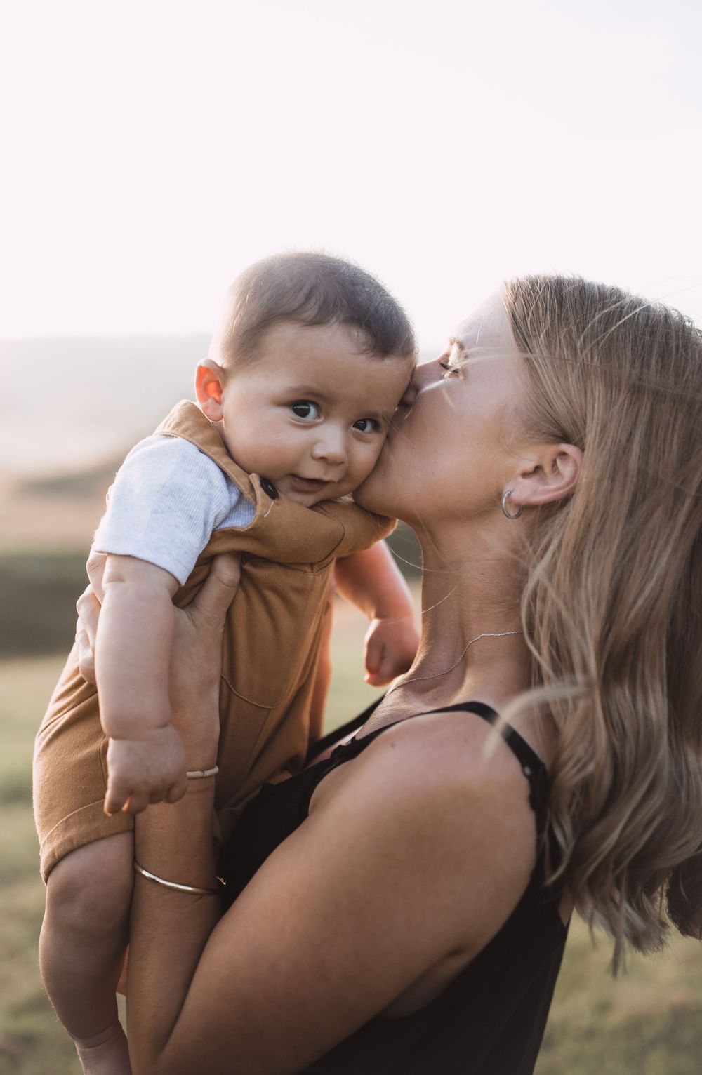 Intimate family portrait showing affectionate moments between parents and baby in warm sunlight.