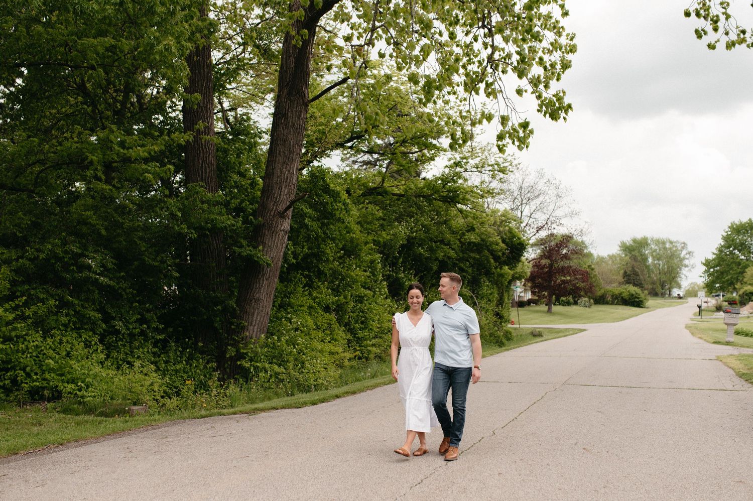 A casual couple walking their dog on a tree-lined suburban street.