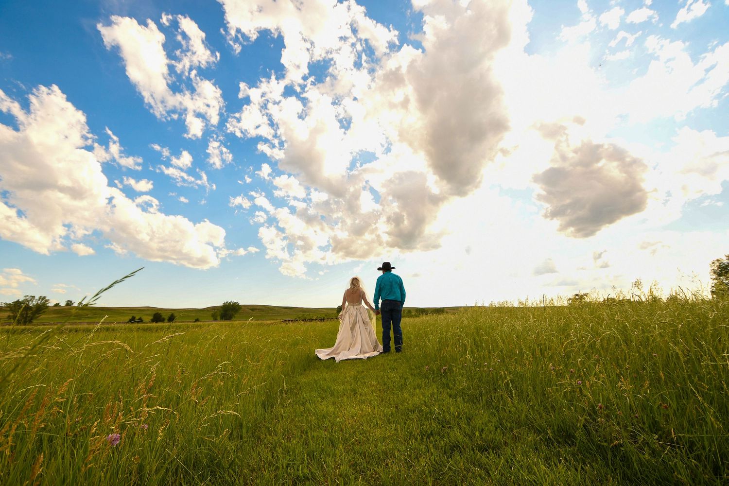 Panoramic view of couple in grassy field under dramatic cloudy sky at sunset.