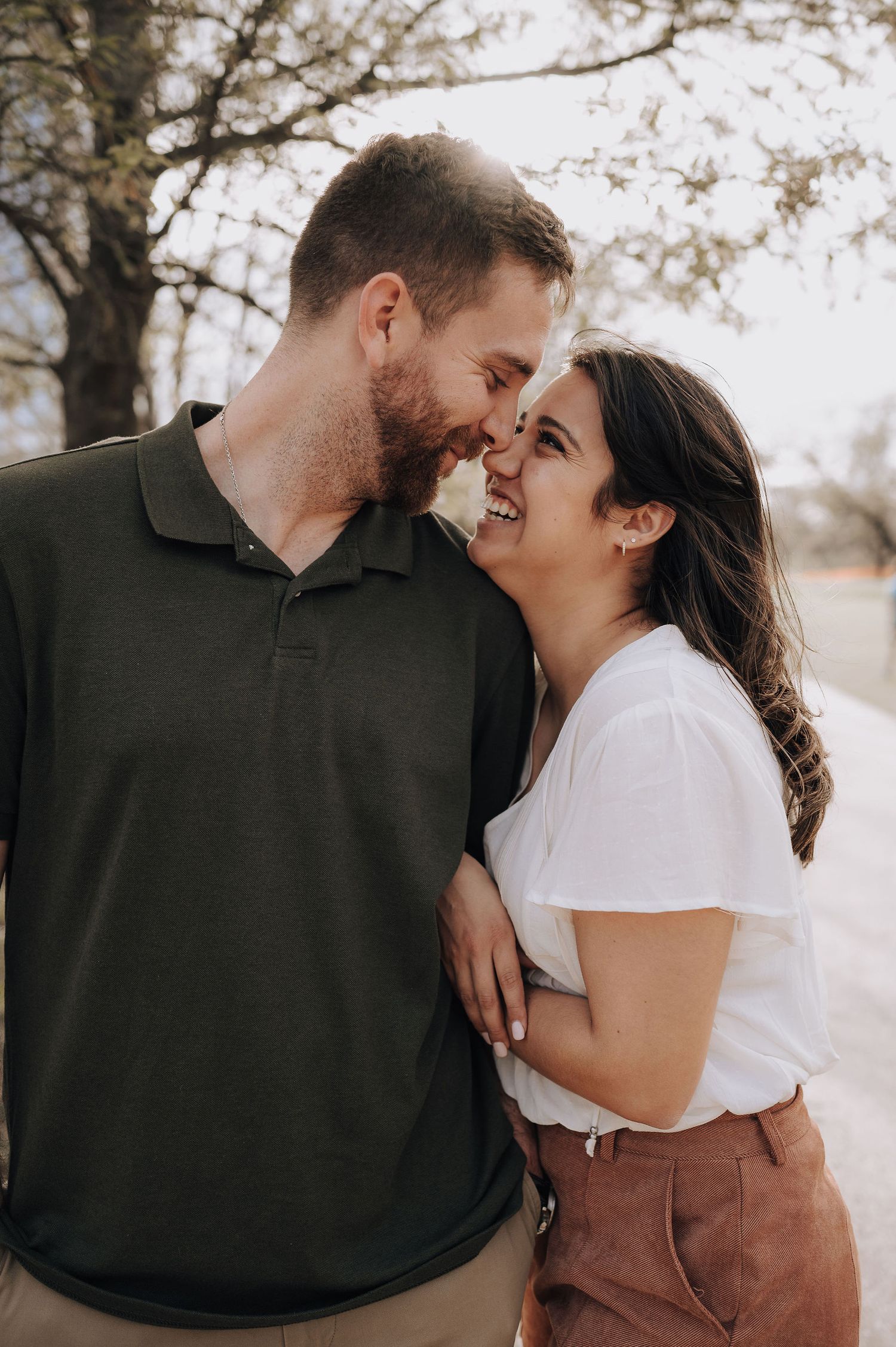 A couple shares an intimate moment while laughing together during their outdoor photoshoot.