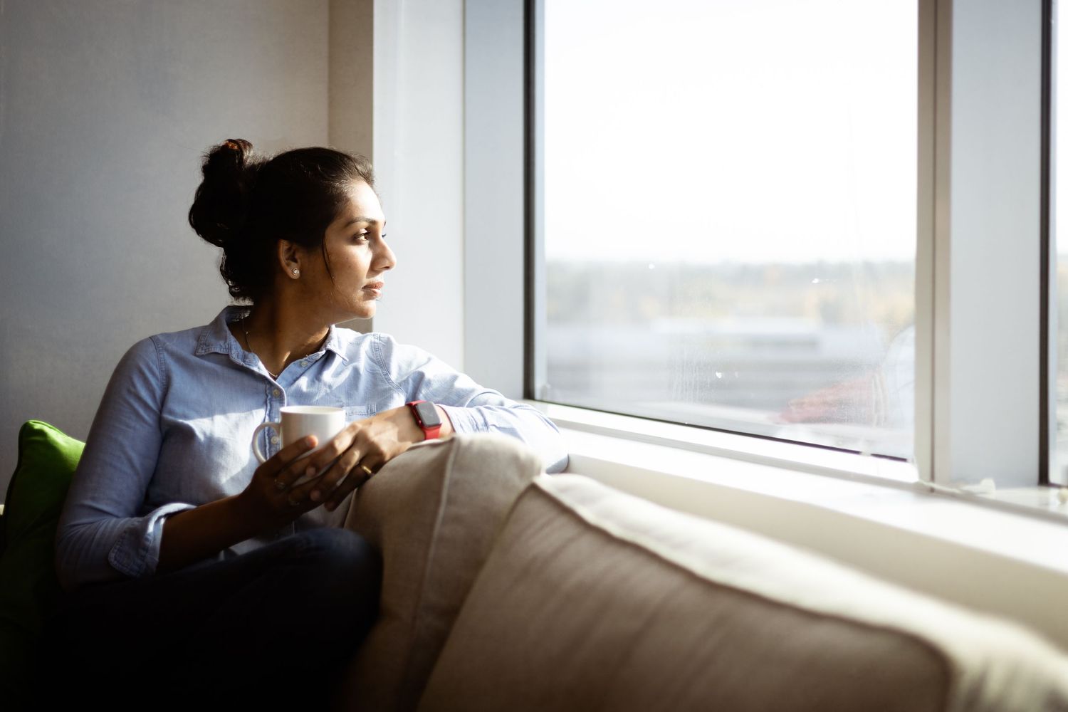 self portrait of a women holding a cup of tea and looking outside the window while sitting on her couch