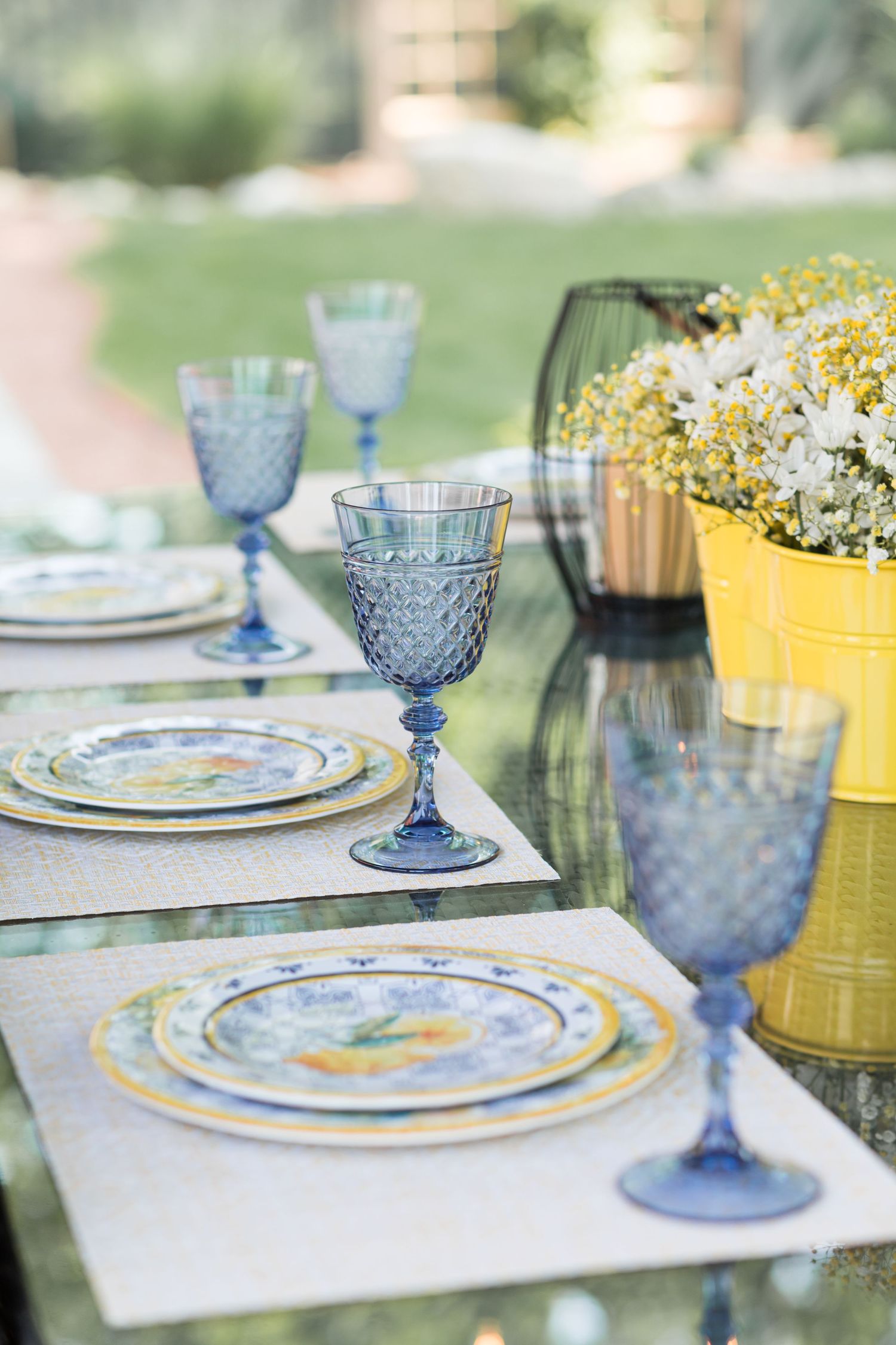Formal table setting with blue stemware, decorative plates, and yellow floral arrangements.