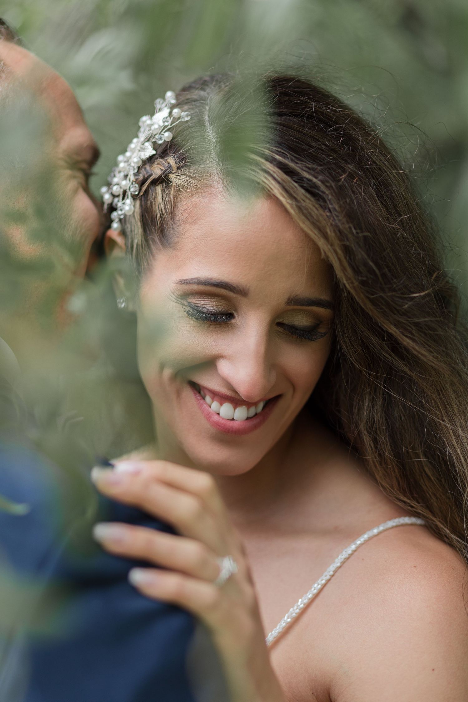 Bride with floral hair accessory smiling with closed eyes in a romantic outdoor setting.