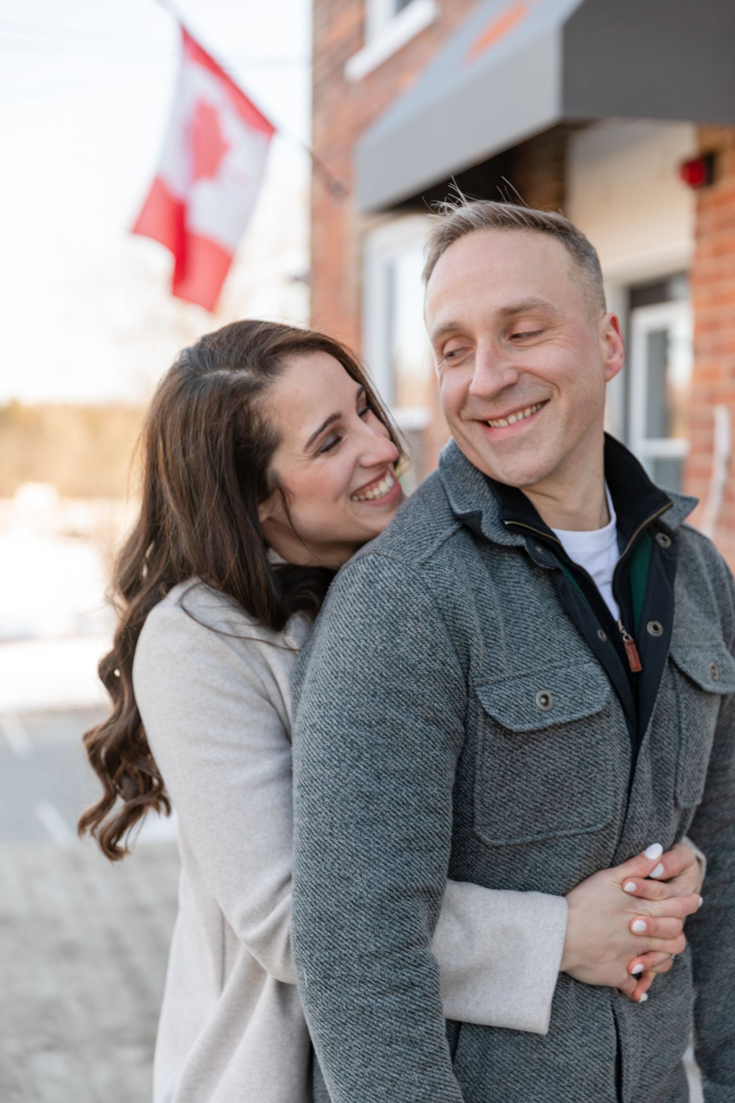 Couple sharing a joyful moment together outside with Canadian flag in background.