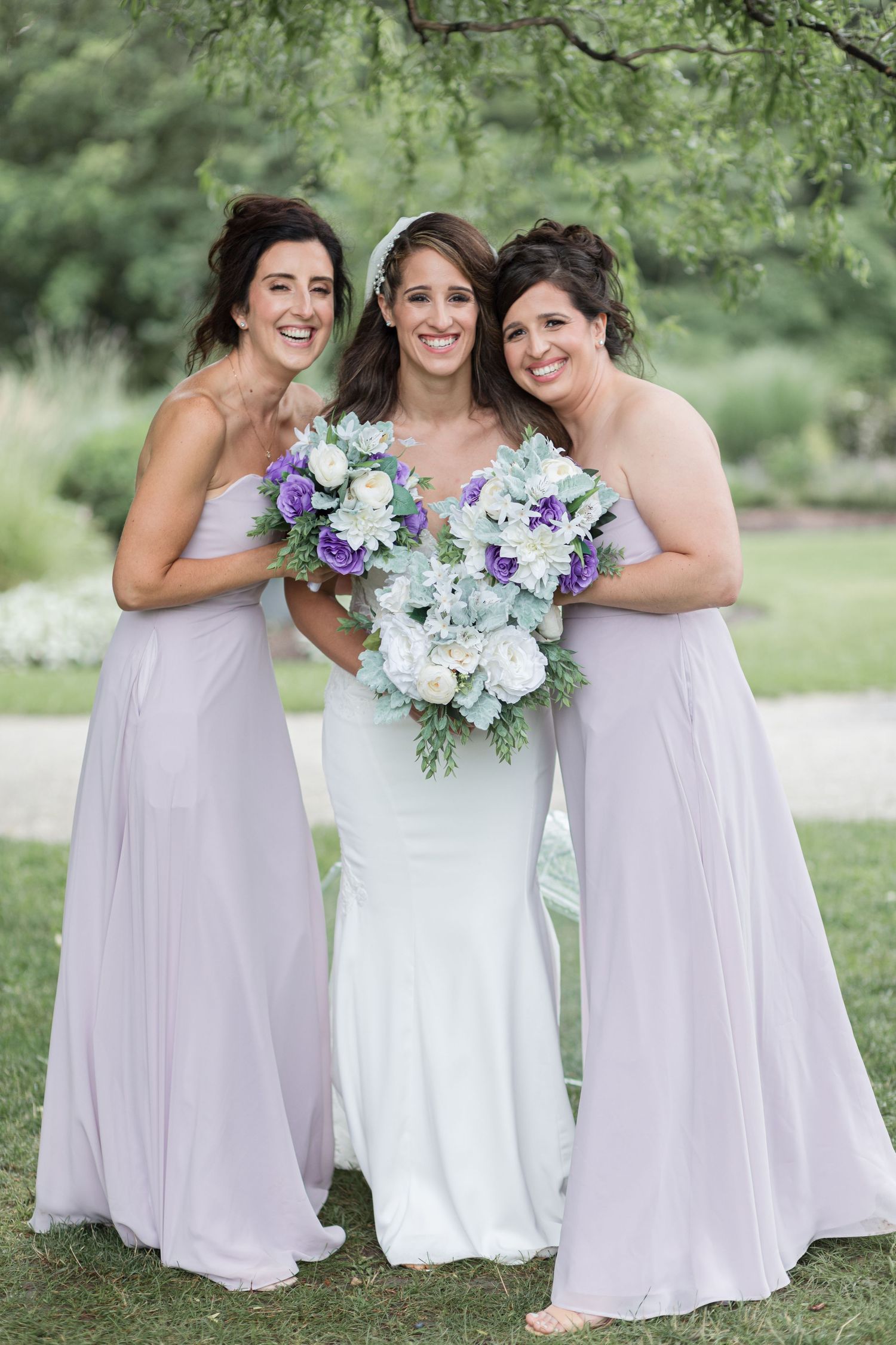 Wedding party in lavender dresses holding elegant purple and white floral bouquets.