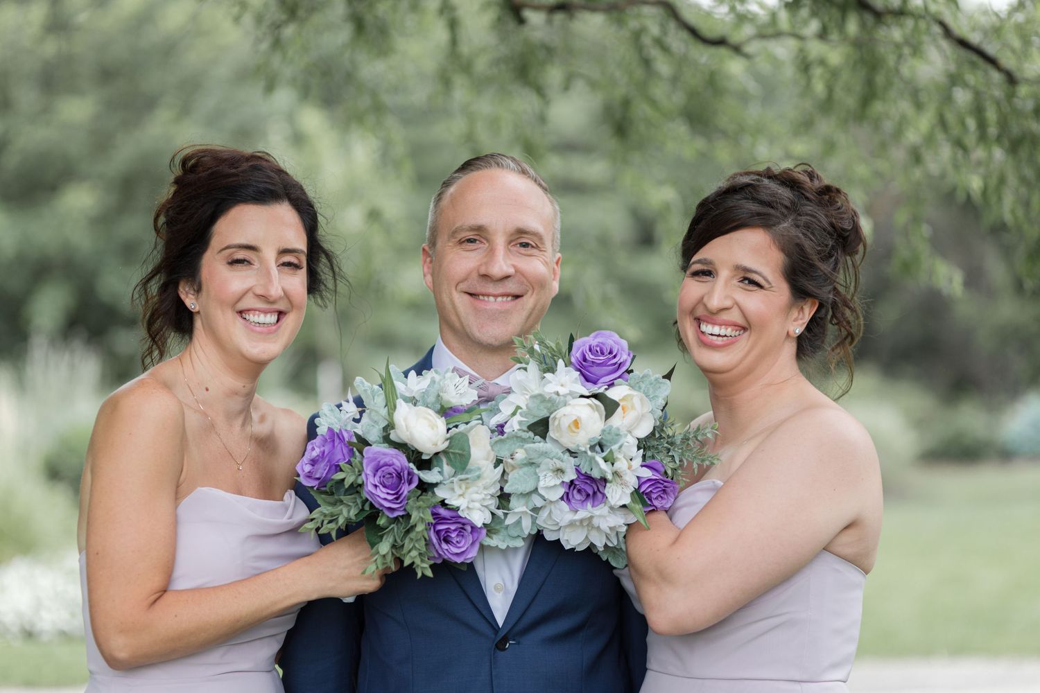 Wedding party with purple and white bouquets posing together outdoors.