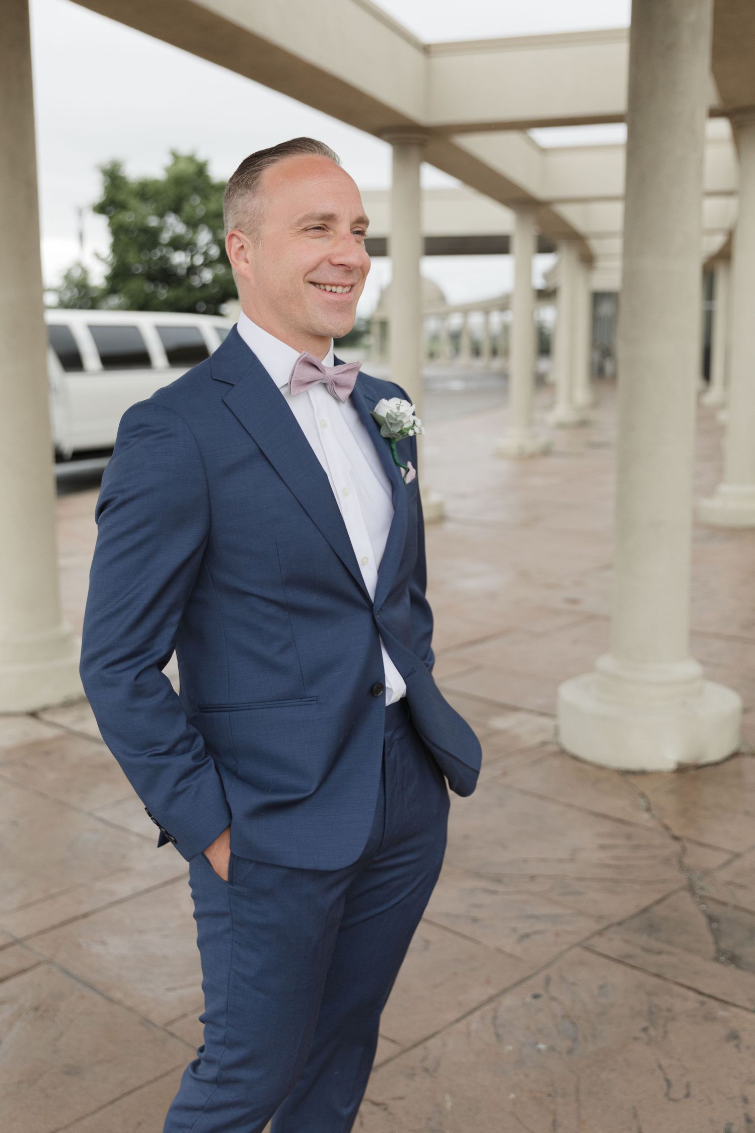 Person in a navy blue suit smiling while standing under a covered walkway.