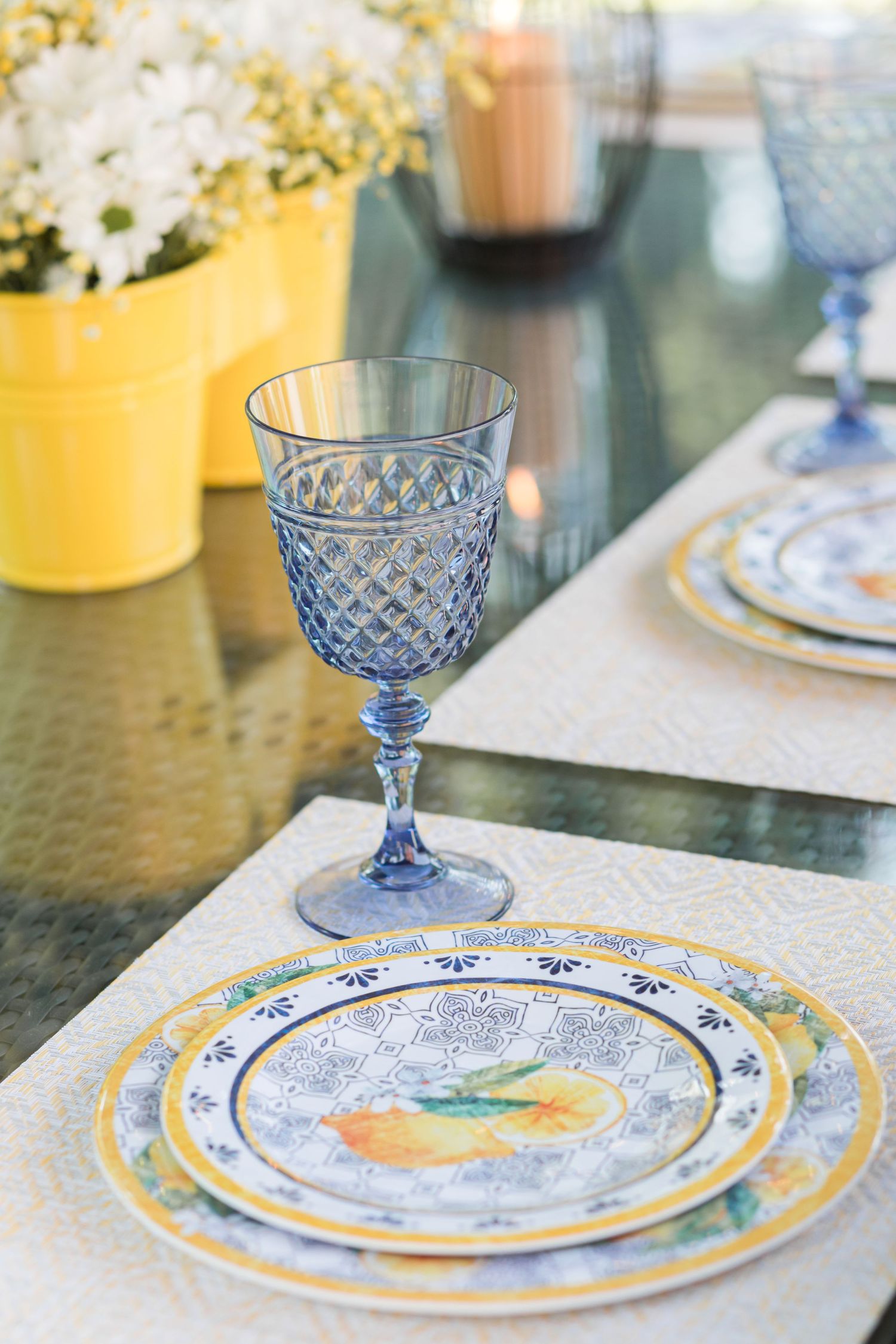 Elegant blue glass goblets and yellow-trimmed plates set on a dining table with floral centerpieces.