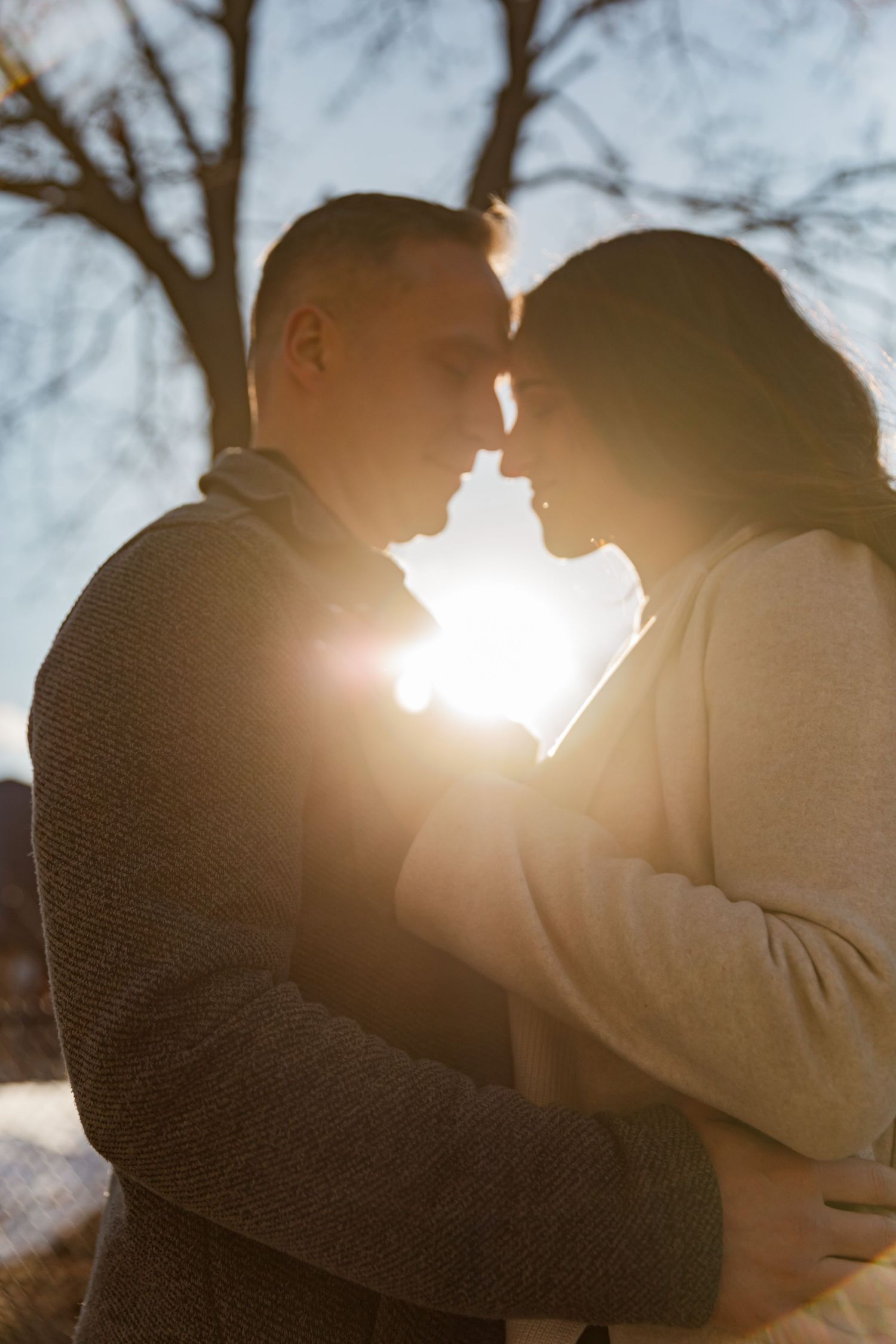 Silhouetted couple sharing an intimate moment against sunlit winter trees.