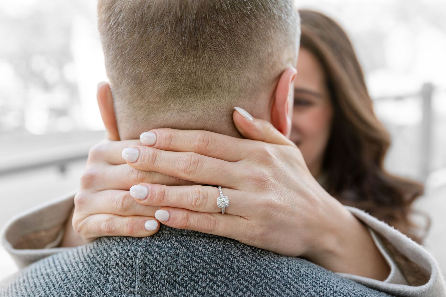 Close-up of hands wearing engagement ring embracing in warm sunlight.