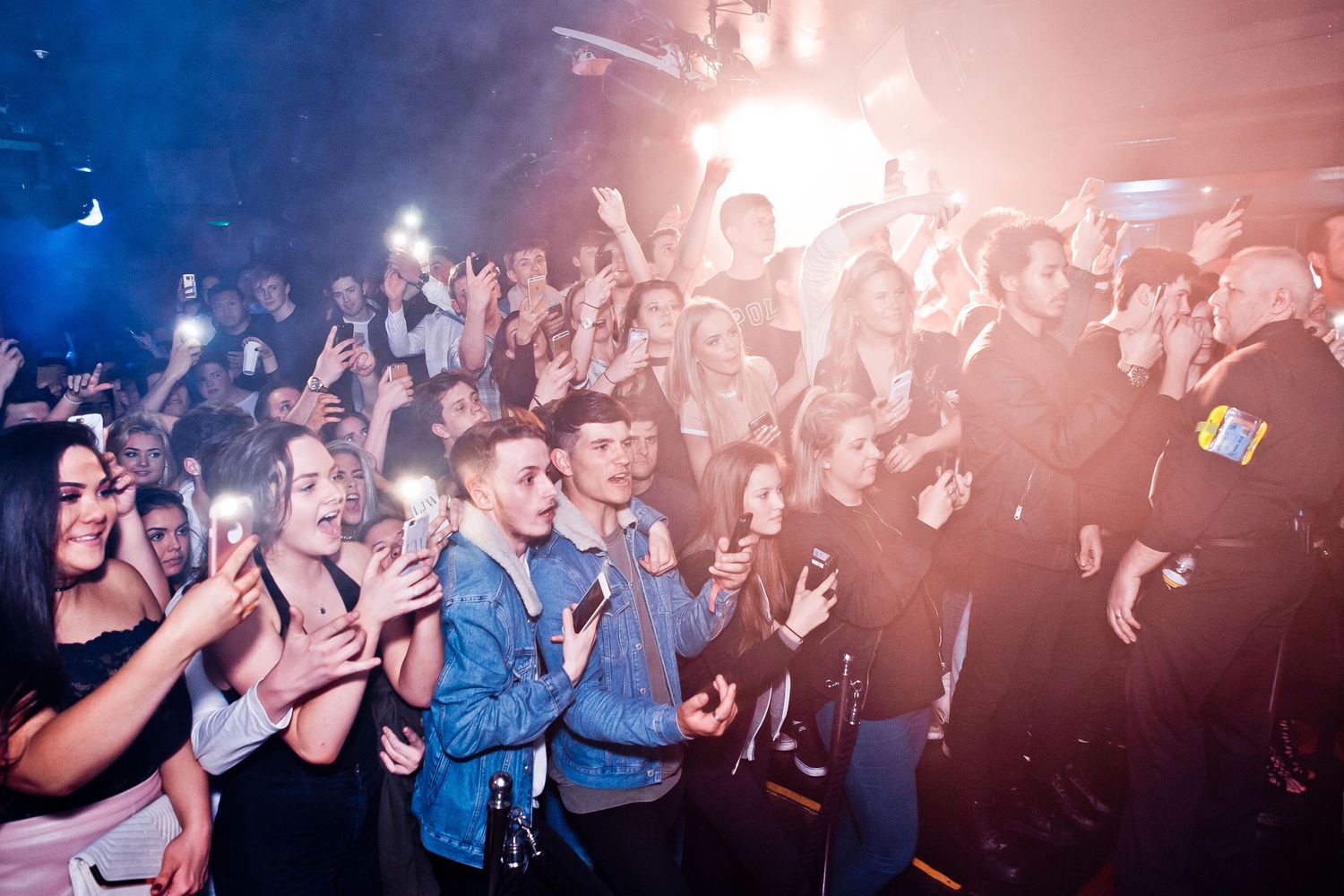 Energetic crowd cheering and dancing at a concert with dramatic lighting effects.