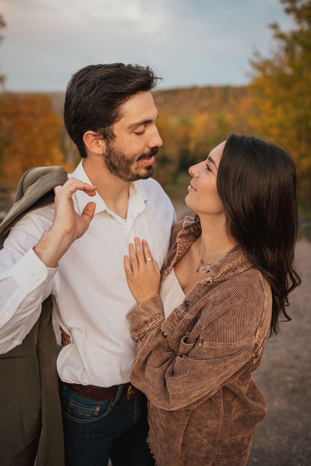 Tender moment between couple wearing white shirt and brown sweater against autumn backdrop.