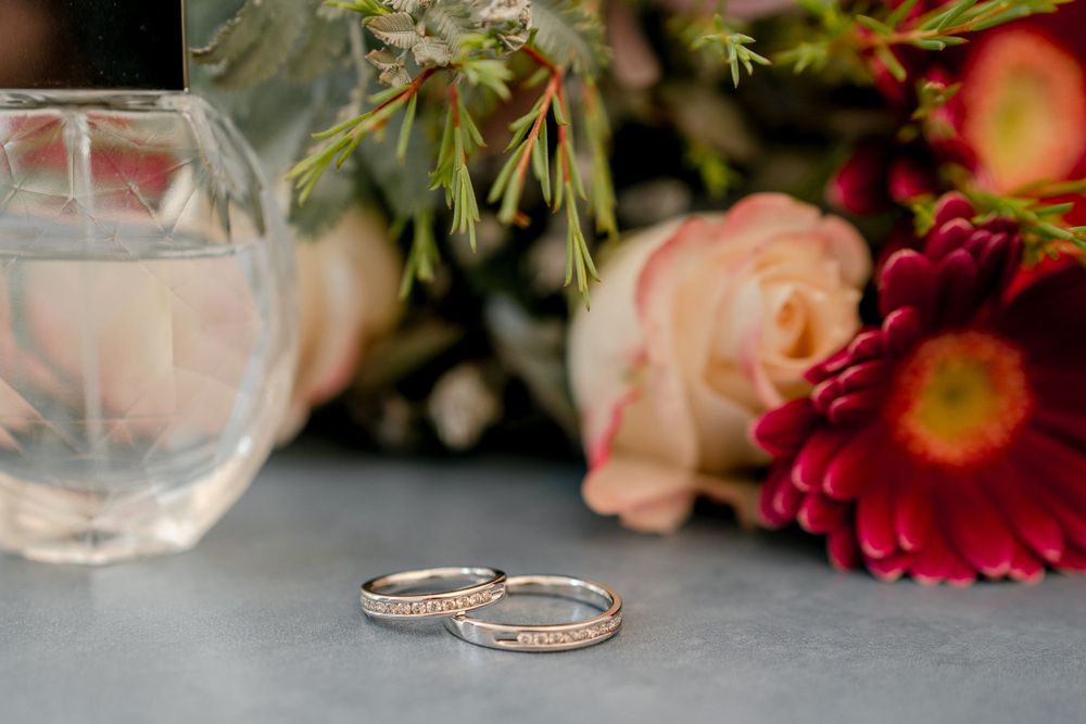 gold wedding rings with diamonds placed in front of floral bridal bouquet and bride's favourite perfume bottle