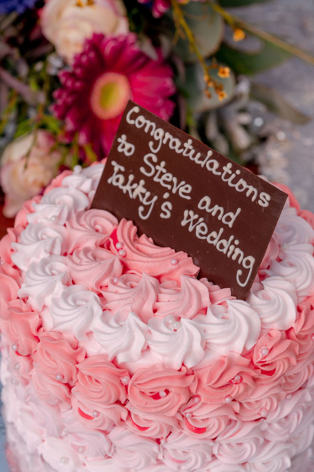 Pink and white rose-decorated wedding cake with chocolate text cards on top.