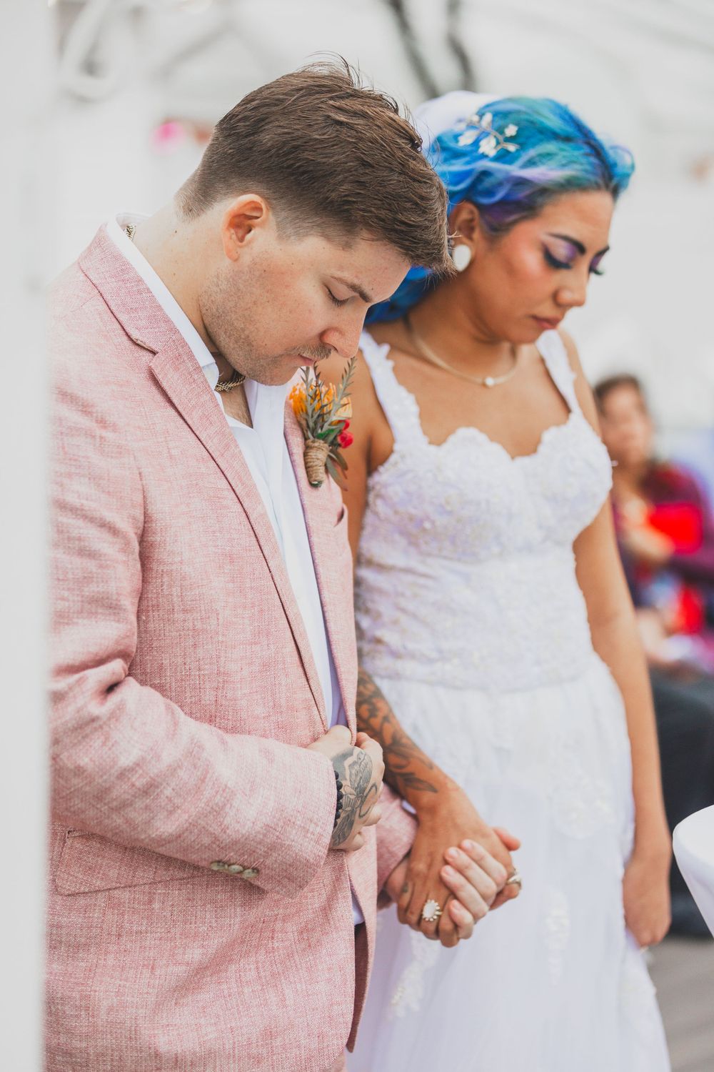 Wedding couple in pink suit and white dress holding hands during ceremony.