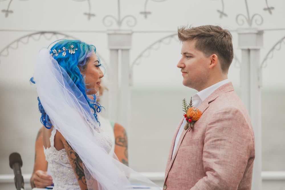 Couple exchanging vows during outdoor wedding ceremony with decorative white lattice backdrop.