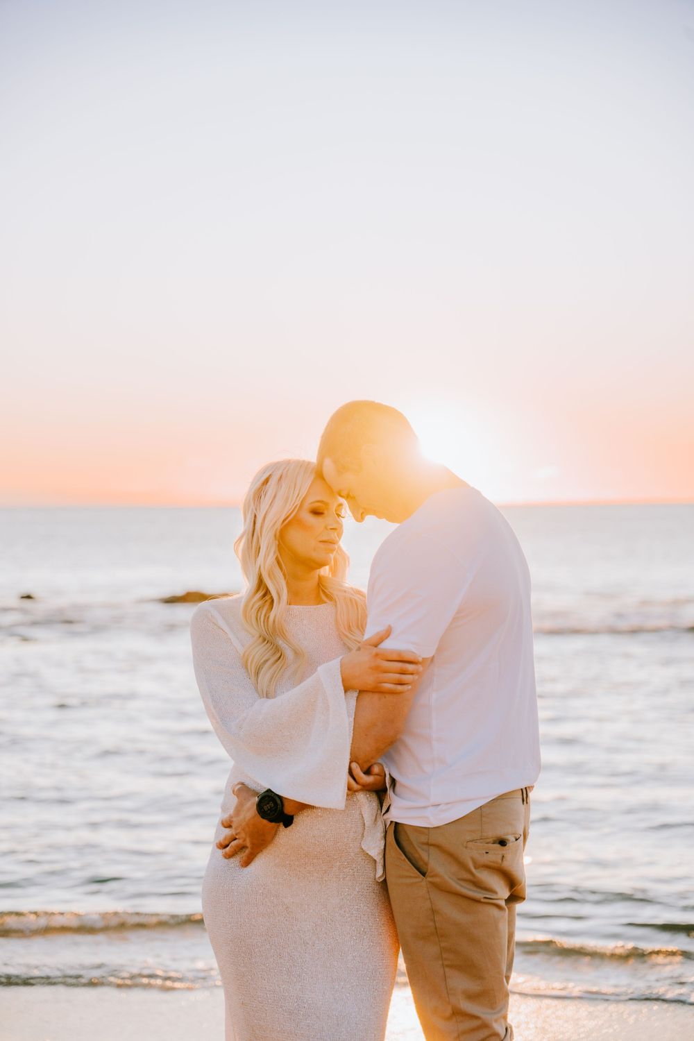 Intimate couple embrace on beach during golden hour sunset.