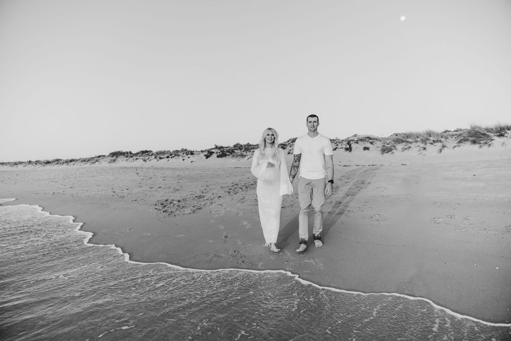 A black and white photo of a couple walking along the shoreline.
