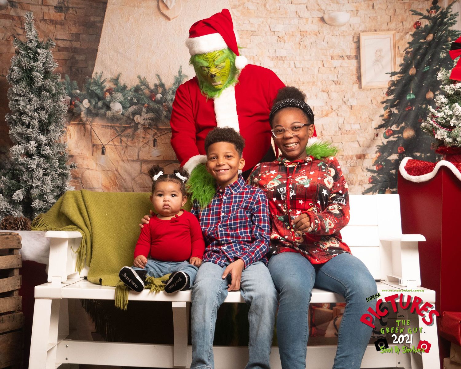The Grinch in Santa costume poses with a group on a white bench during a holiday photo session.