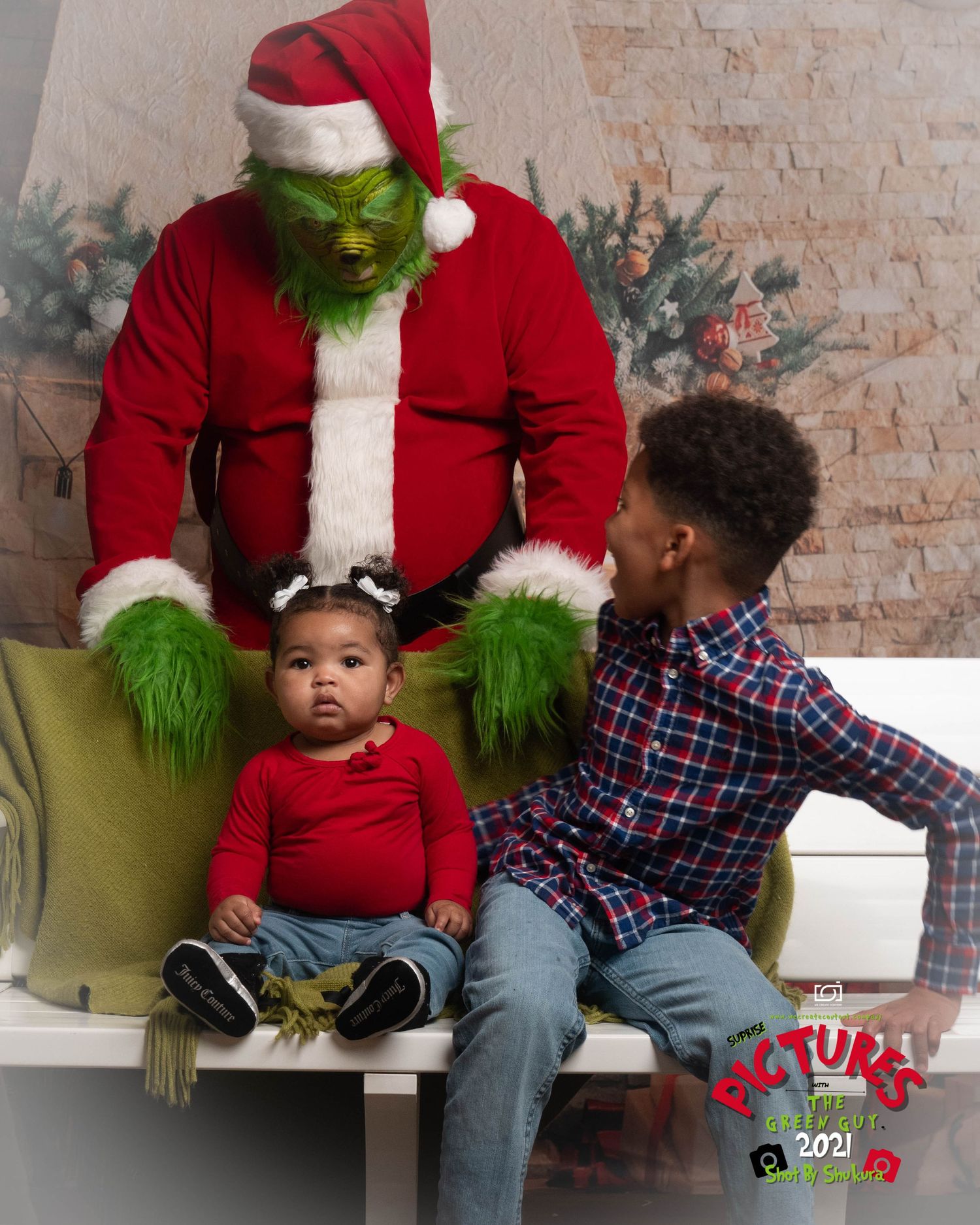 The Grinch in Santa costume sits with two children on a white bench during a Christmas photo shoot.