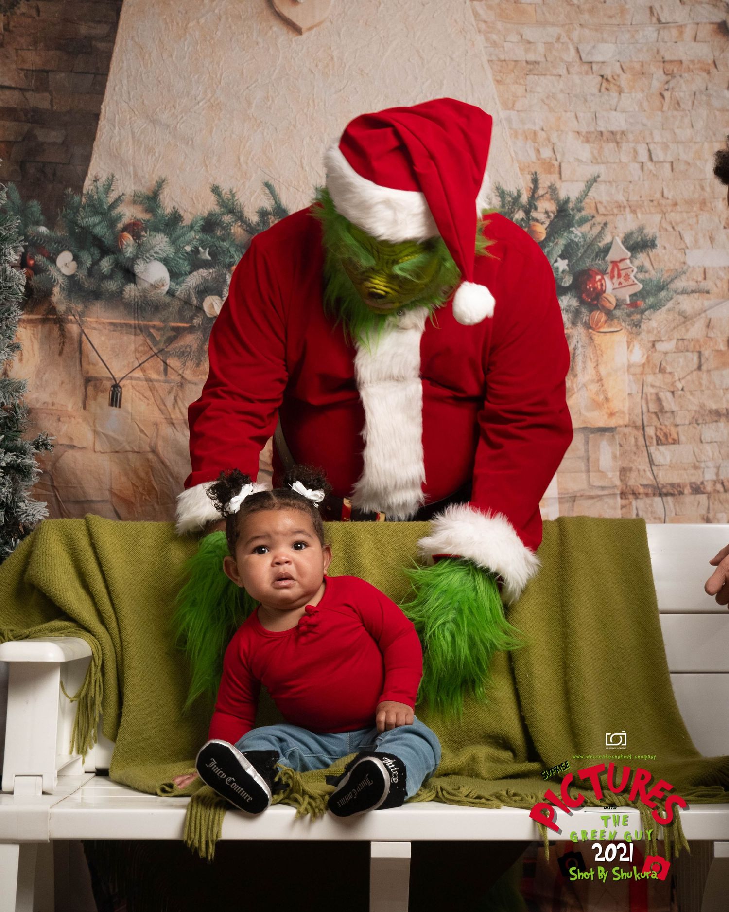 A small child in red sits next to the Grinch dressed as Santa during a holiday photo session.