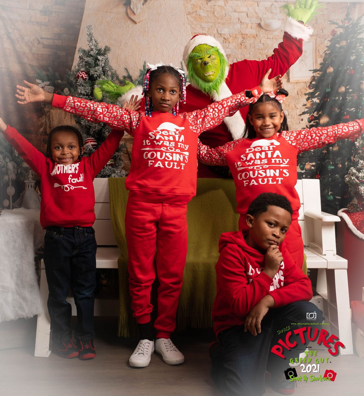 A group wearing matching red holiday outfits poses energetically with someone in a Grinch costume against a festive backdrop.