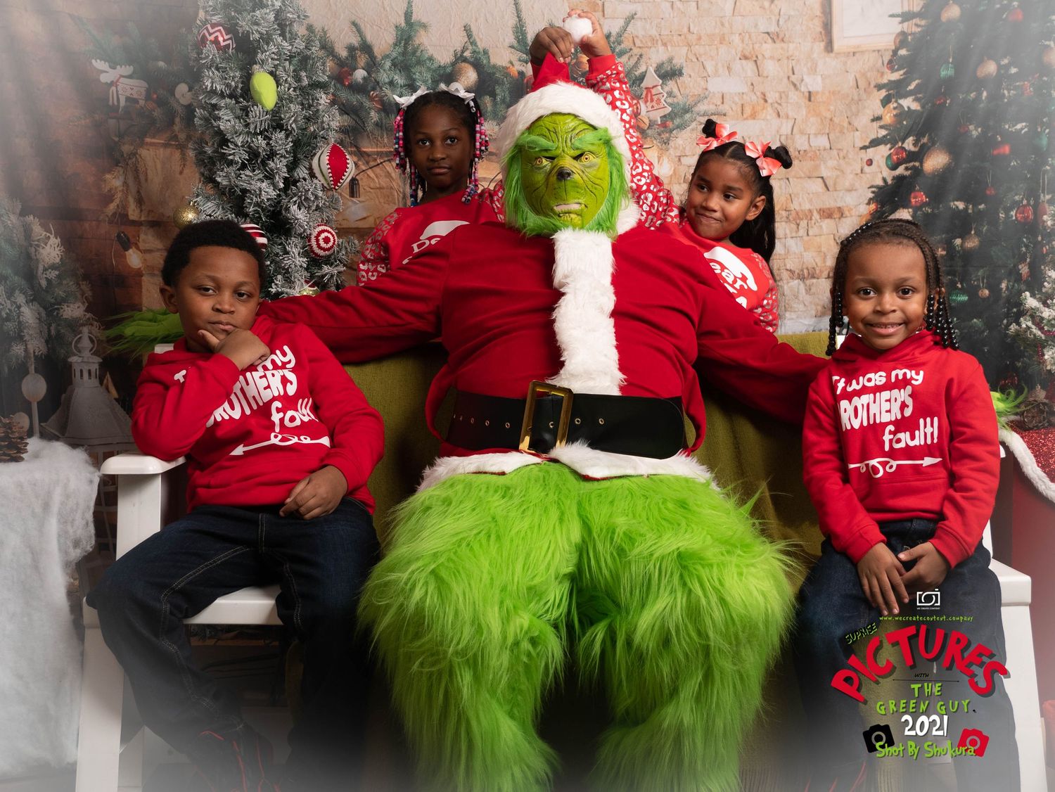 The Grinch in a Santa suit poses with children wearing matching red holiday sweaters in a festive Christmas setting.