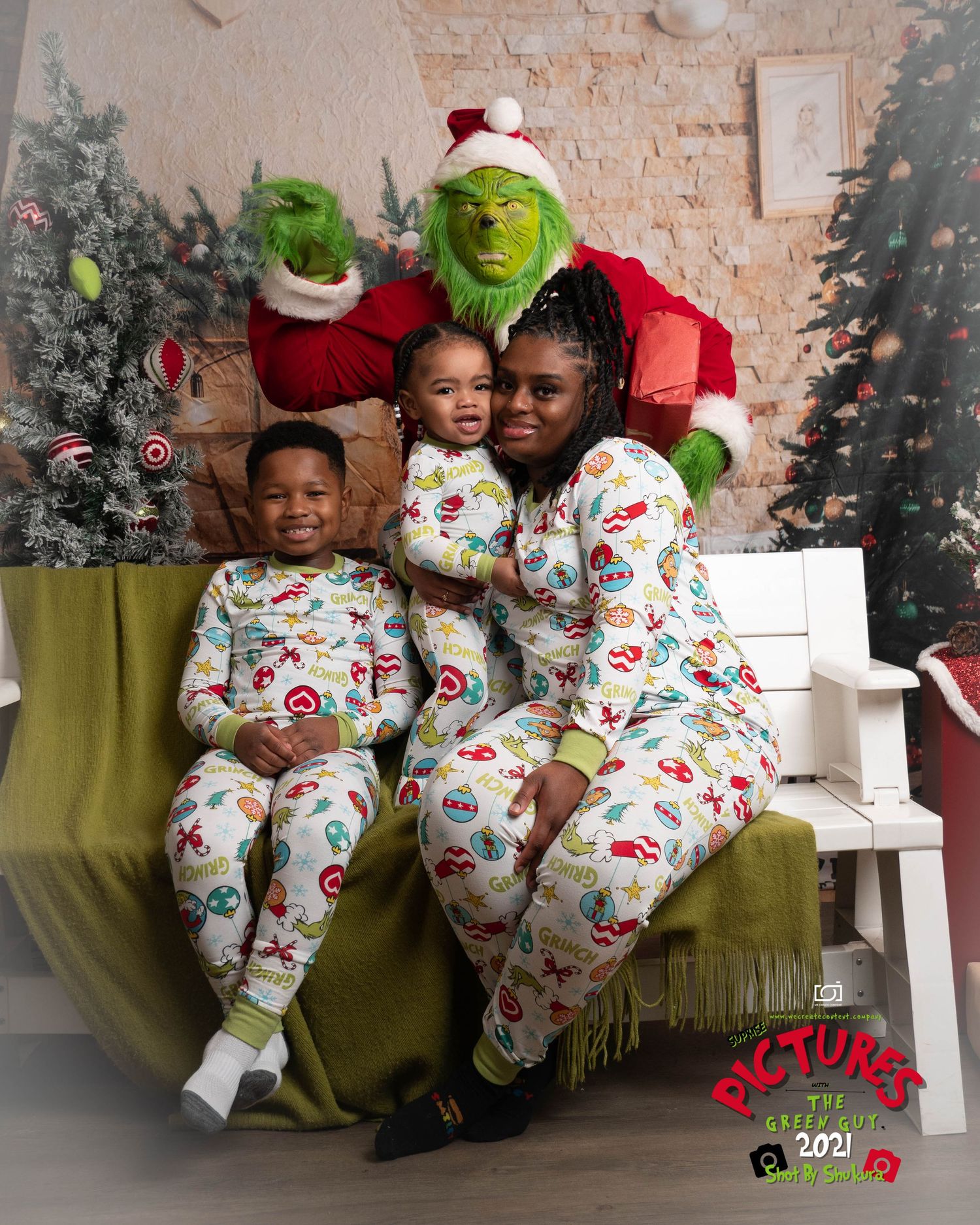 A group wearing matching Christmas pajamas poses with someone in a Grinch costume on a festive holiday set.