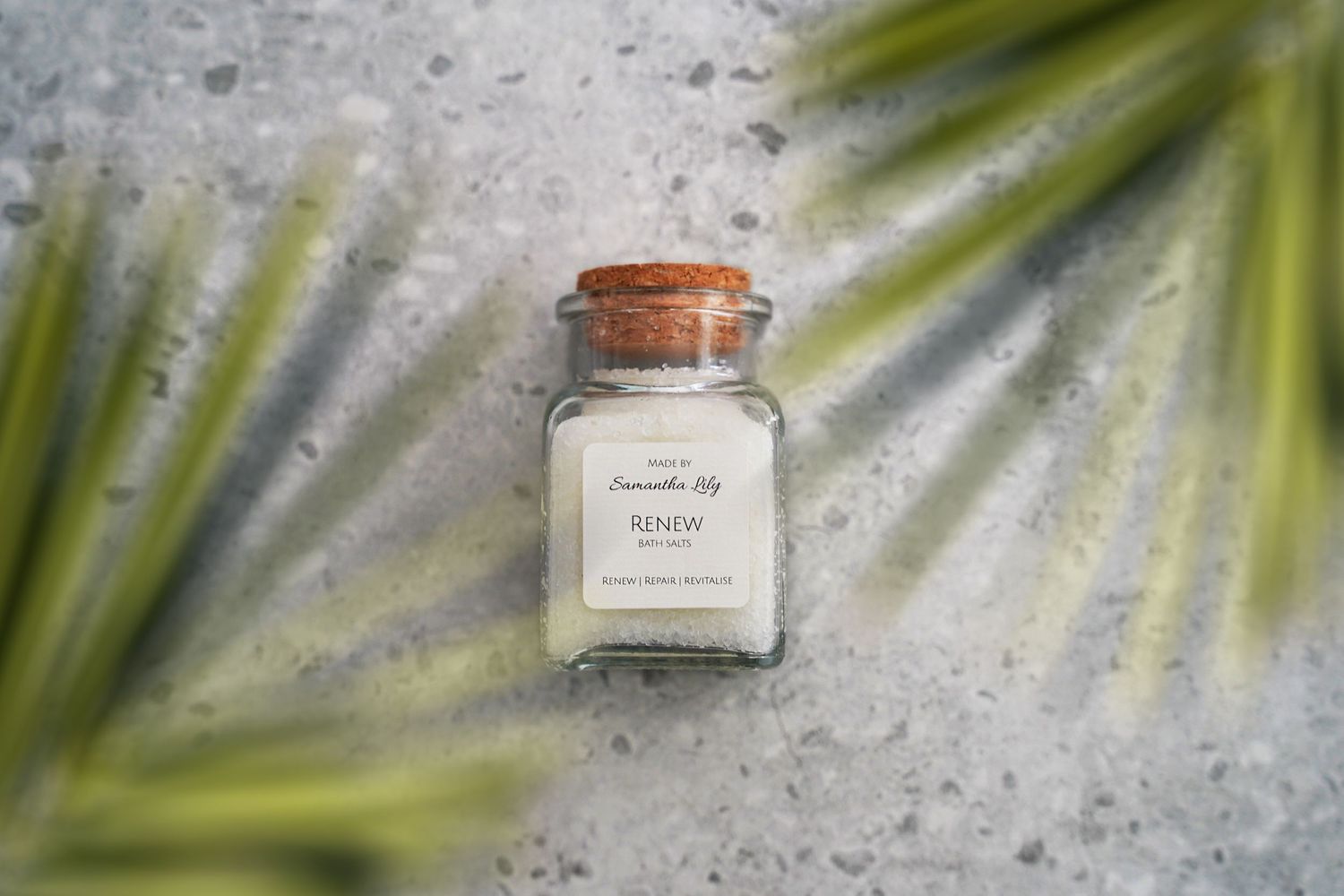 Glass cosmetic jars with copper lids arranged against palm leaves and gray background.