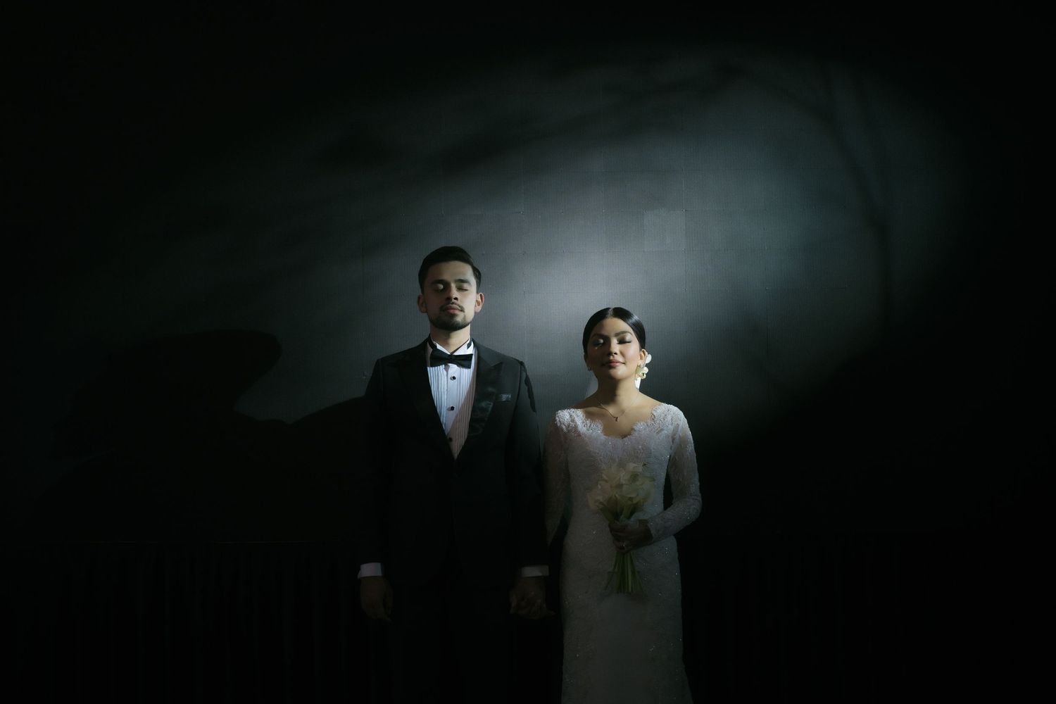 Dramatic portrait of a wedding couple in formal attire illuminated against a dark moody background.