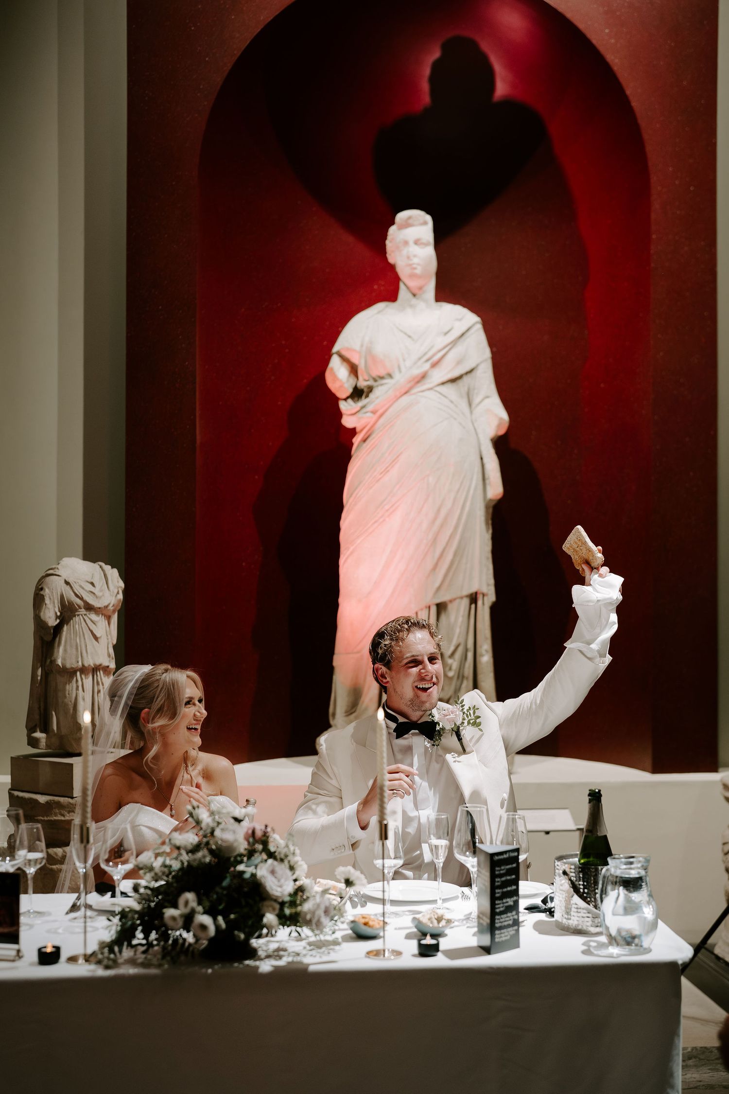 groom waving a piece of toast during best man speech in the grand sculpture gallery at the Ashmolean Museum