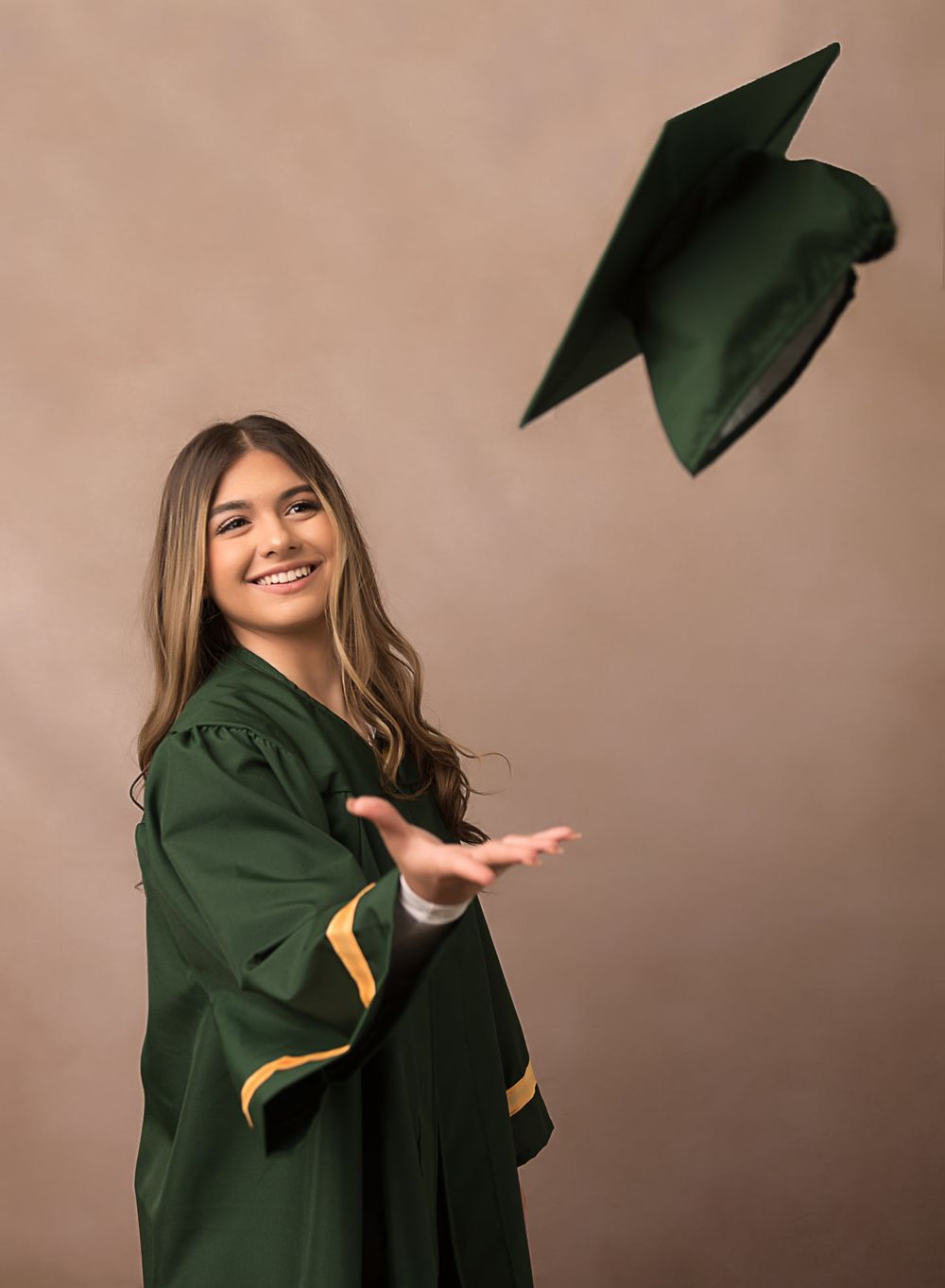Graduate in green regalia tossing cap in celebratory graduation photo.