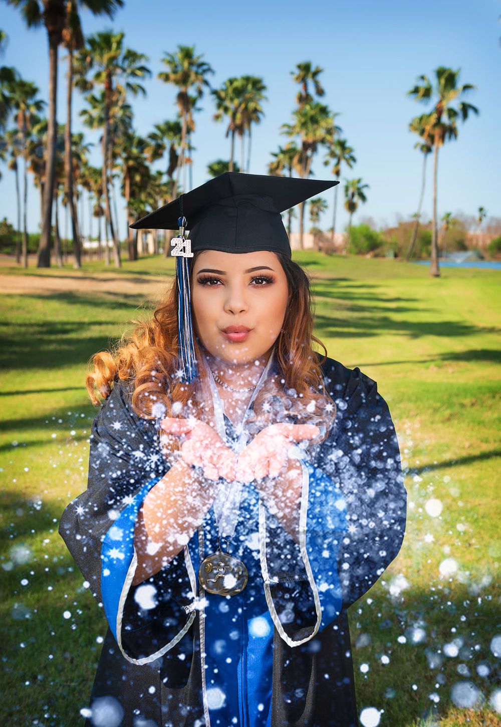 Graduate blowing glitter with magical effect in outdoor graduation photo.