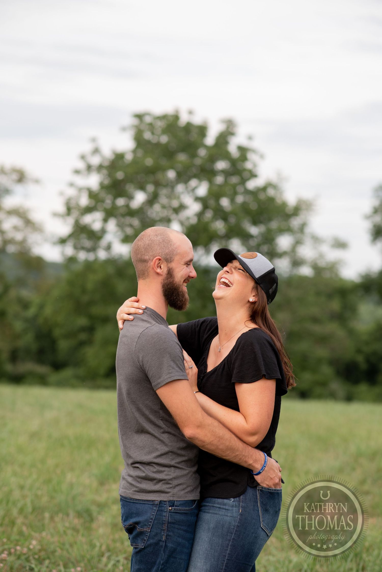 A couple sharing genuine laughter while embracing in a grassy field.