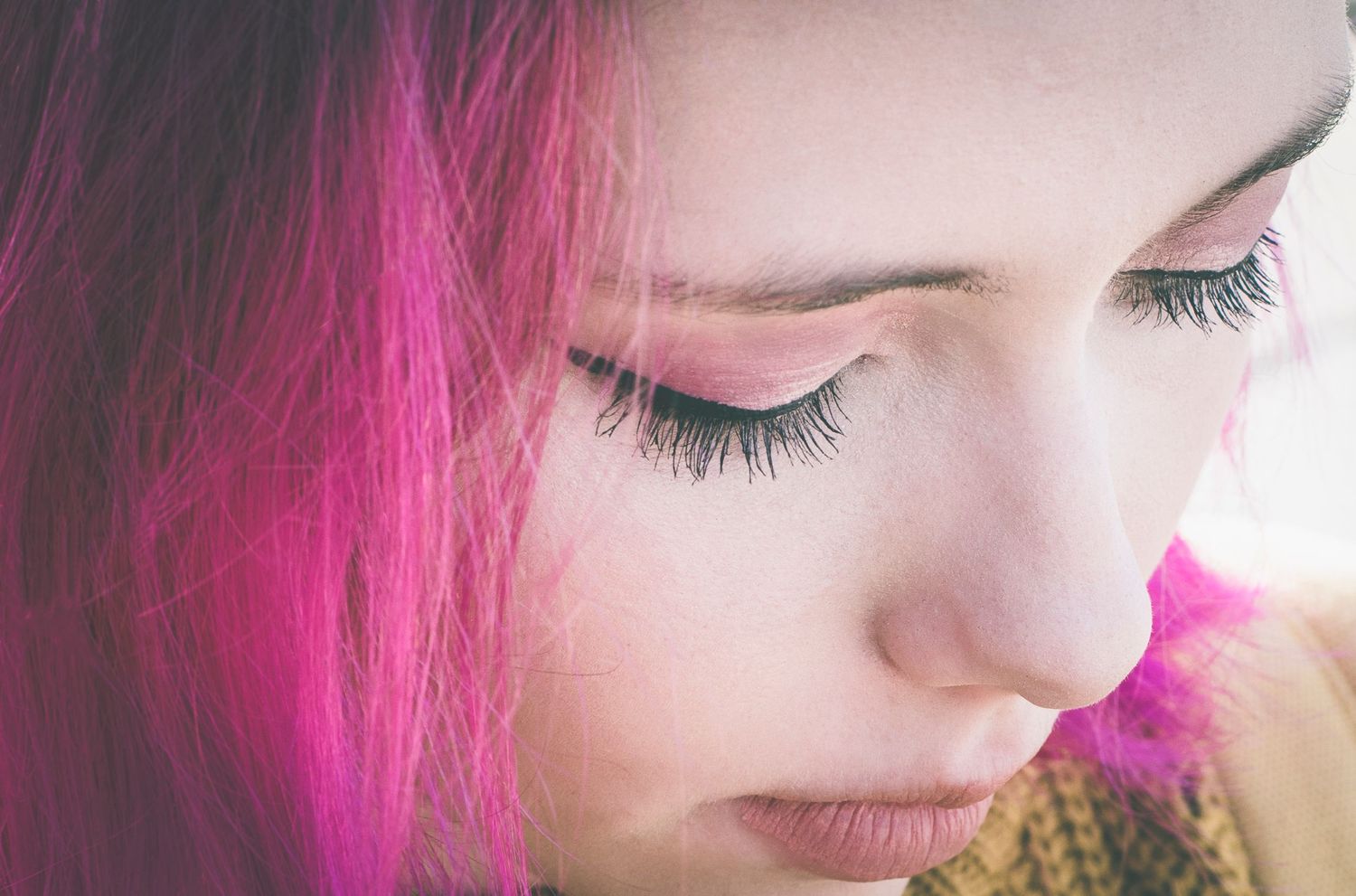 Close-up portrait of a young woman with vibrant pink hair and long eyelashes.