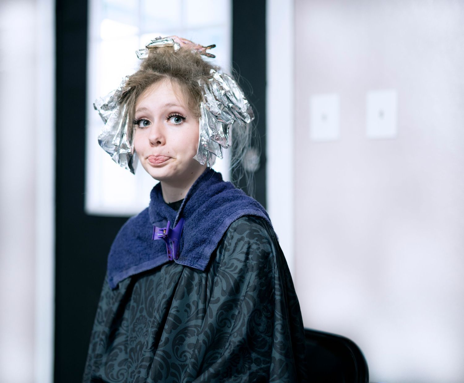 Young woman with foil hair treatment makes a funny face at a hair salon.