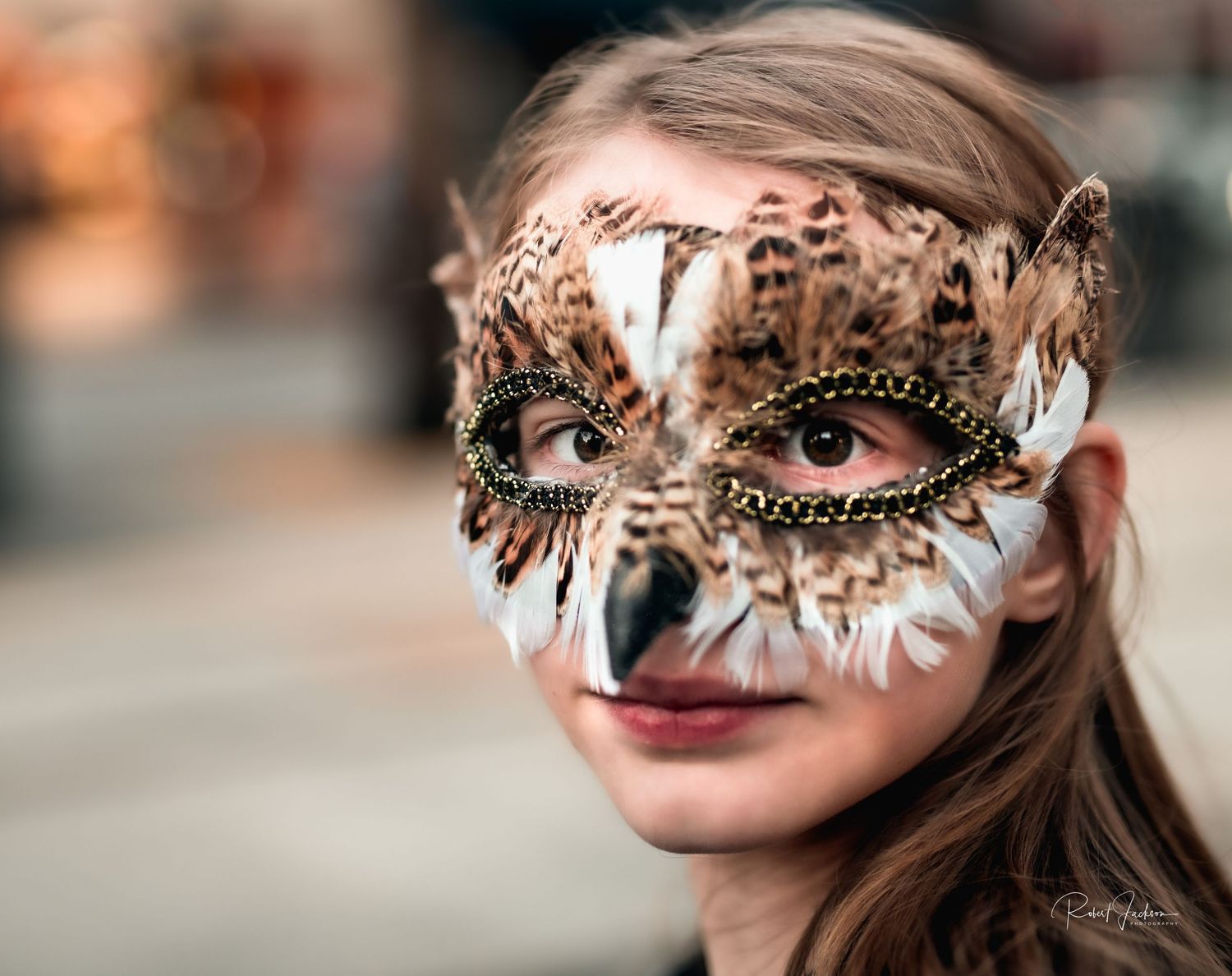 Young girl wearing an ornate feathered owl masquerade mask outdoors.