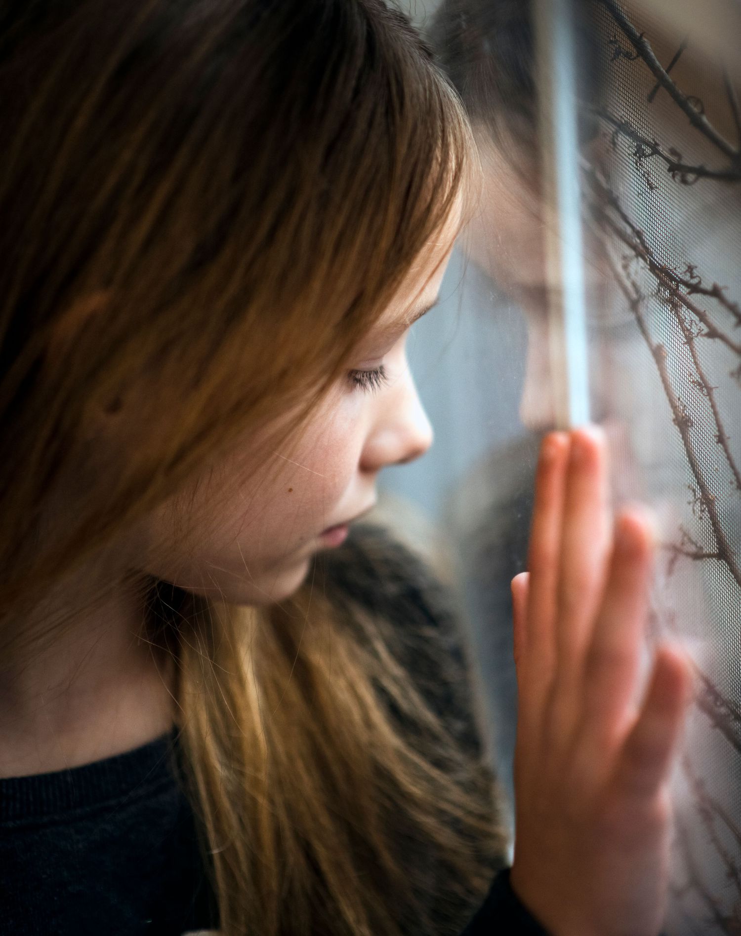 Young girl with brown hair gazing thoughtfully through a rain-streaked window.