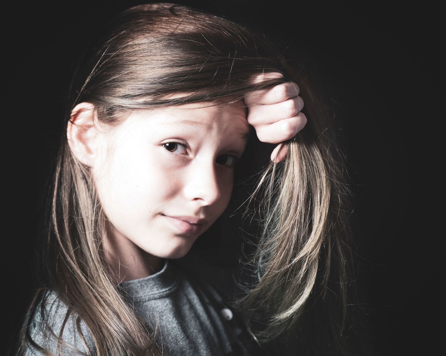 Young girl with long brown hair holding hair back in moody dark portrait.