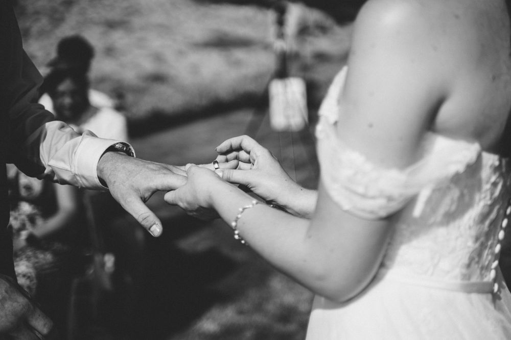 Black and white shot of couple exchanging rings at outdoor wedding.