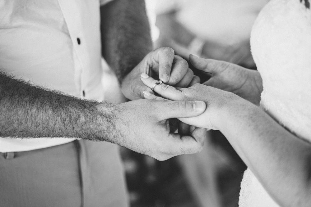 Black and white close-up shot of hands during wedding ring exchange.