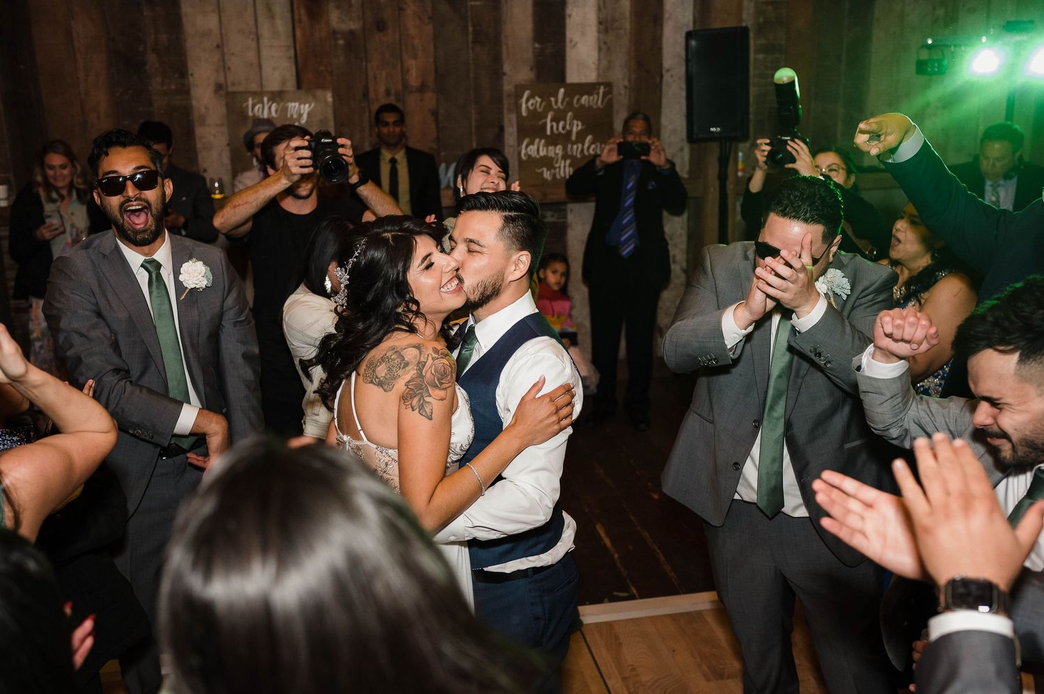 Lively wedding reception party with guests dancing and clapping in a rustic venue.