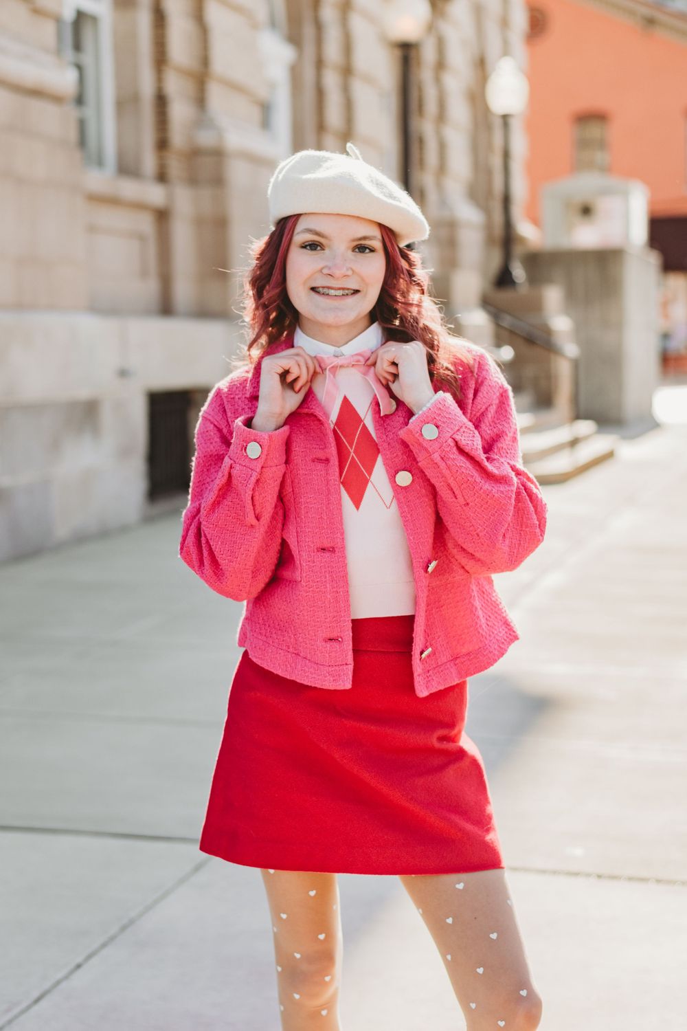 Playful fashion poses in pink jacket and red dress against light stone building.